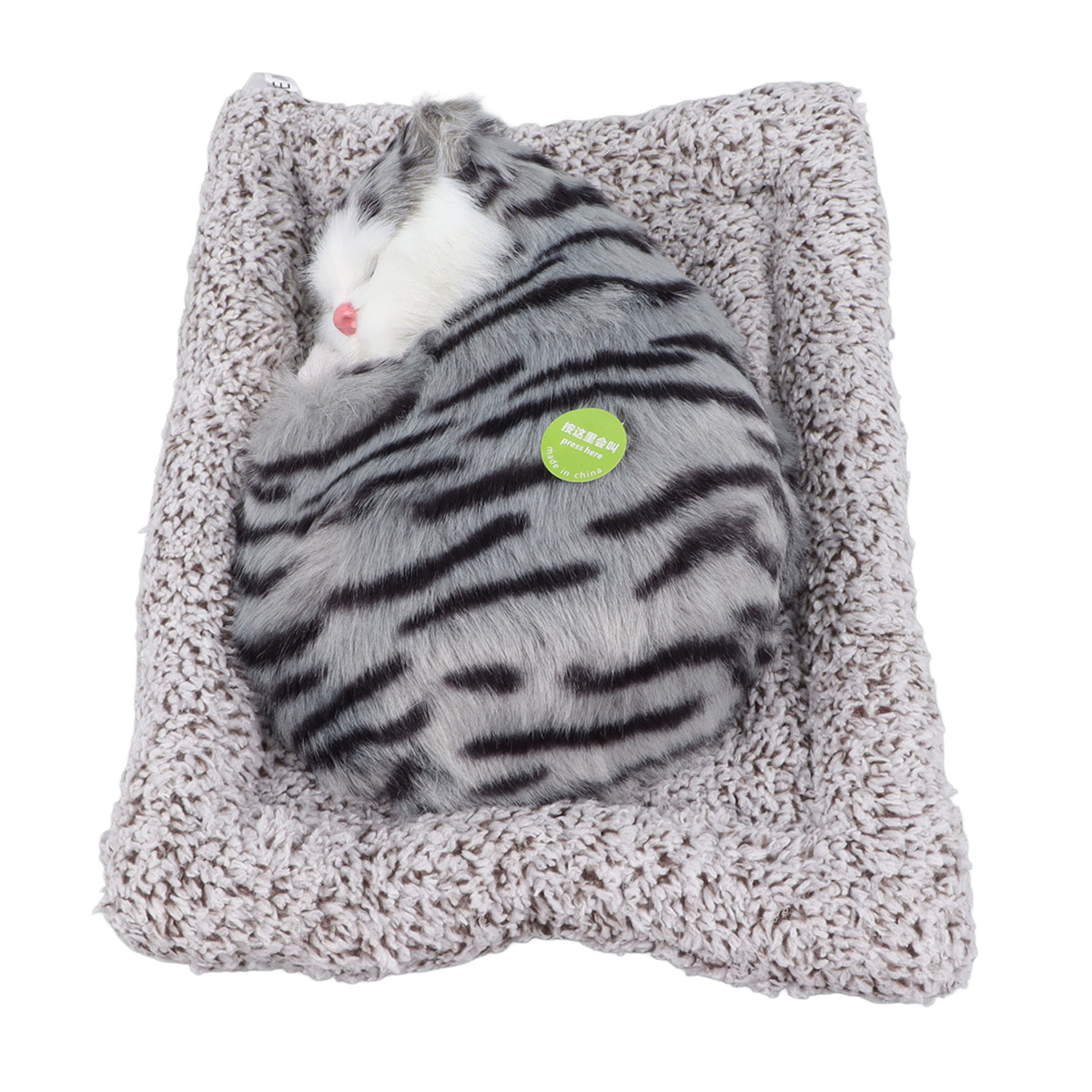 Katzen-Plüschtier schläft auf grauem Bett, Streifenmuster, grünes Etikett.