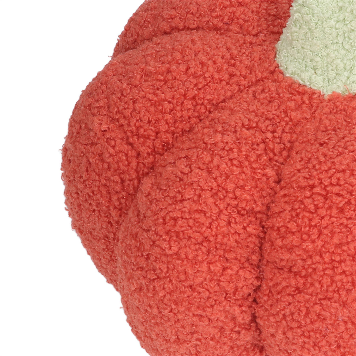 Nahaufnahme eines zotteligen, orangefarbenen, kürbisförmigen Kissens. Oben ist ein grünes Blatt sichtbar.
