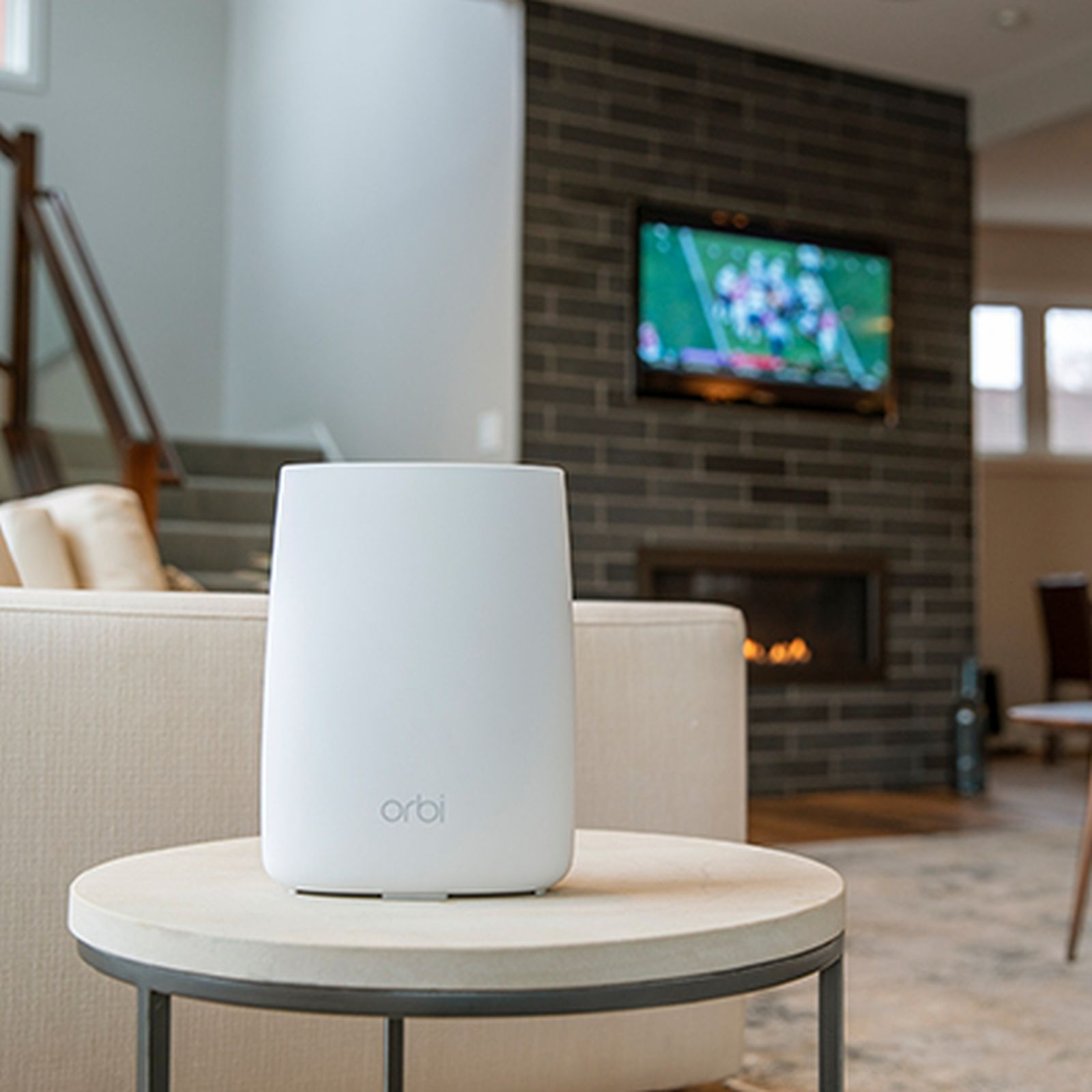 Un router wifi bianco su un tavolo con una TV sullo sfondo.