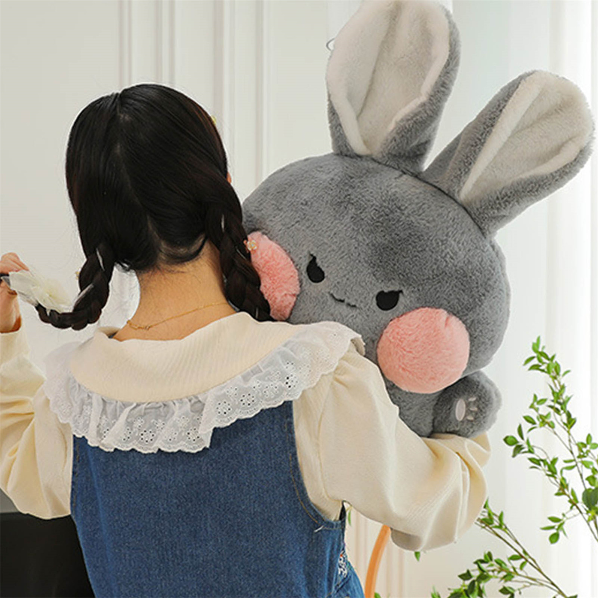 Eine Frau hält ein graues Hasenplüschtier. Der Hase hat rosa Wangen und lange Ohren. Die Frau trägt ein Jeanshemd.