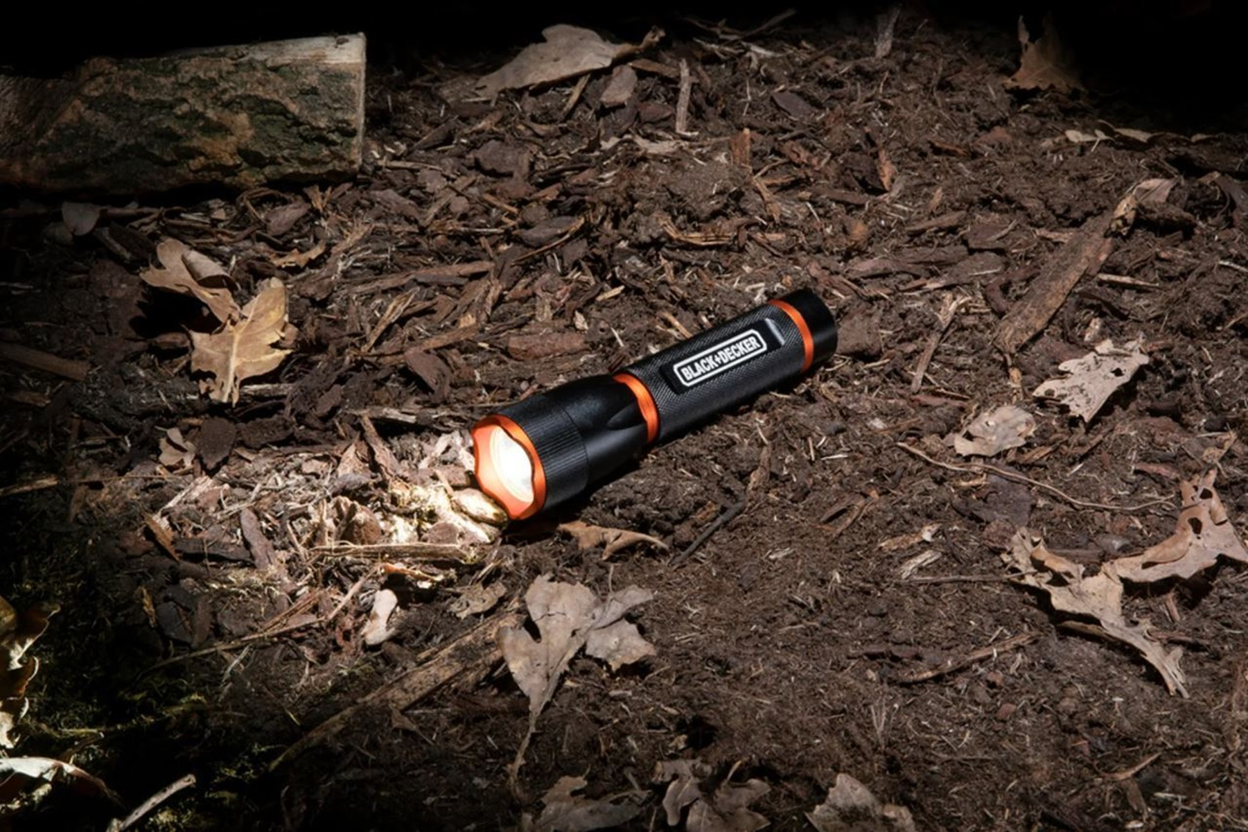 Zwarte zaklamp die licht uitstraalt op de grond. Hij ligt in het donker op een bed van bladeren en mulch.