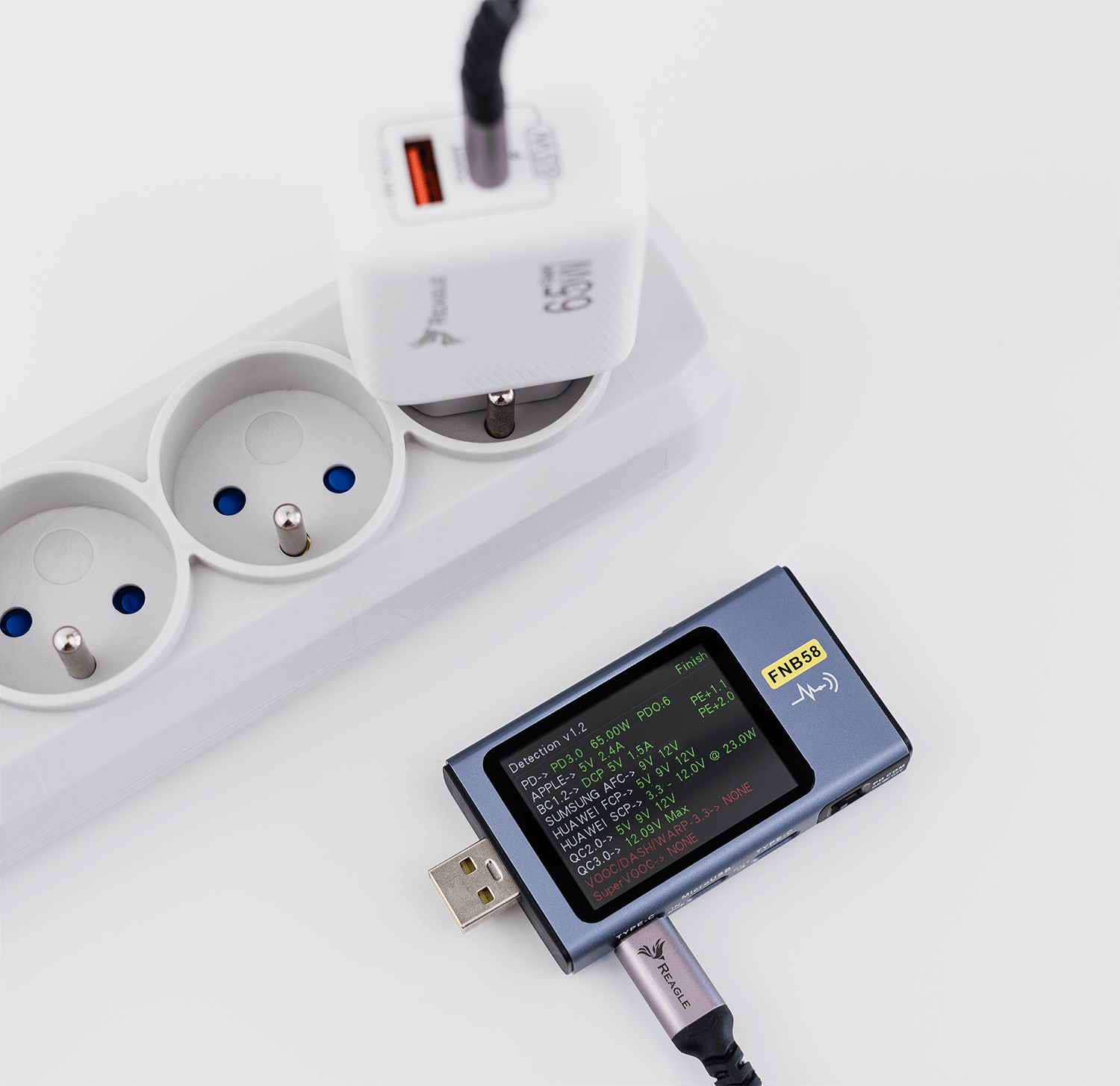 Zasilacz, listwa zasilająca i urządzenie ładujące. Tło białe.