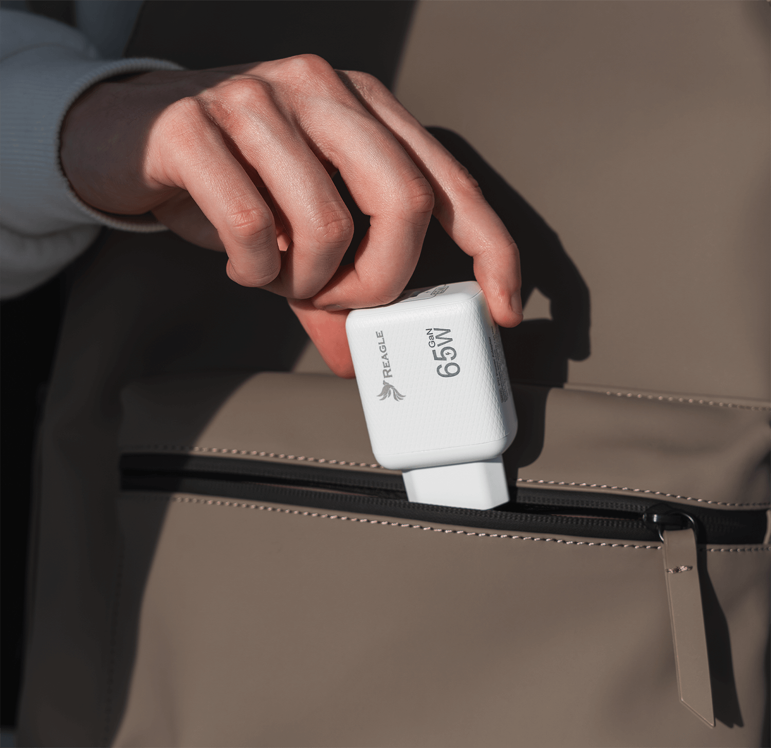 Dłoń trzymająca białą ładowarkę 65W, częściowo w beżowej kieszeni.