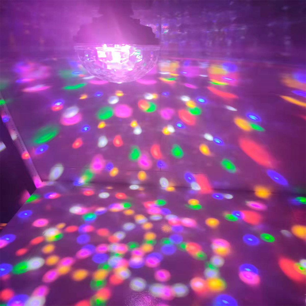 Eine Discokugel wirft bunte Lichter auf einen Boden. Das Bild wird von rosa Licht beleuchtet.
