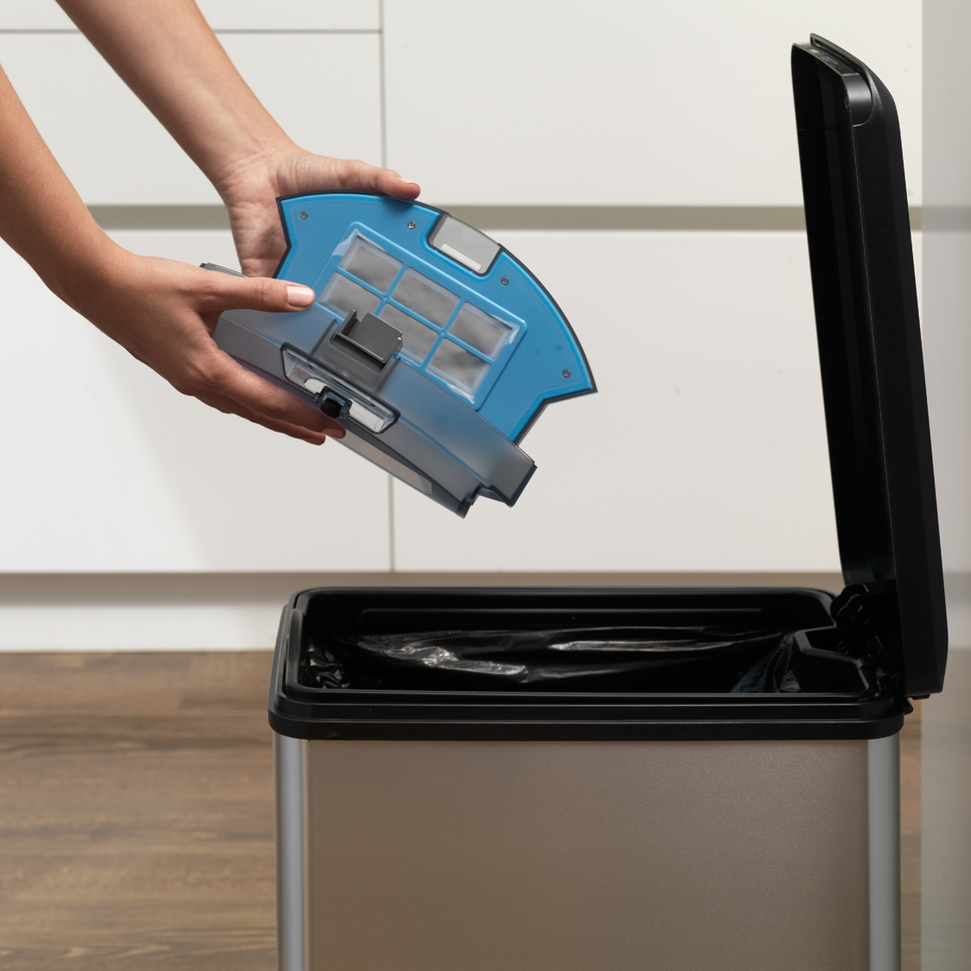 Manos de una mujer quitando un filtro azul de un cubo de basura. Bolsa de basura negra visible.