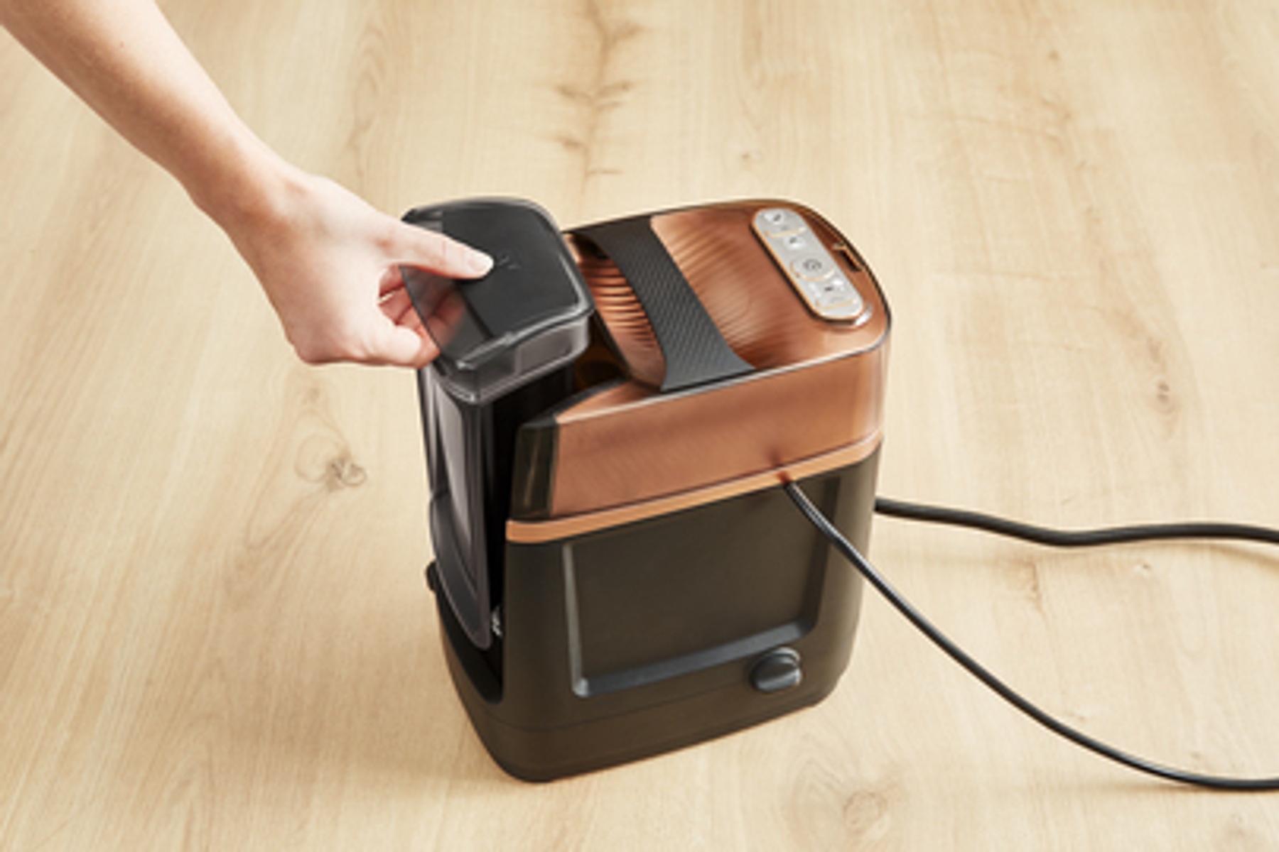 Ręka osoby wyjmująca czarny pojemnik z miedziano-czarnego urządzenia, prawdopodobnie parowaru.