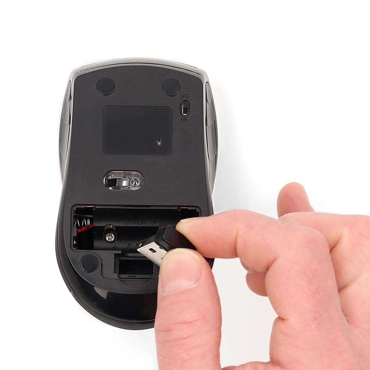 A person's hand is putting a USB receiver into the back of a black computer mouse.