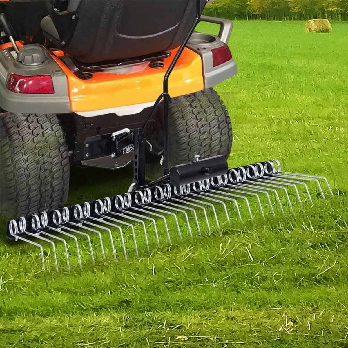 Ein Rasenharkenzubehör an einem Aufsitzmäher auf grünem Gras. Die Harke hat mehrere Zinken.