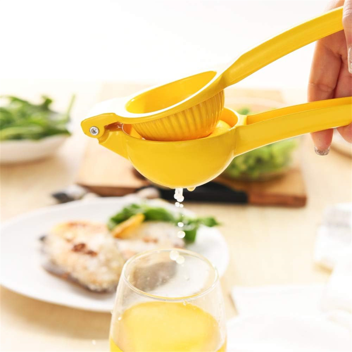 Ein gelber Zitrus-Entsafter, der Saft in ein Glas presst, mit Essen im Hintergrund.