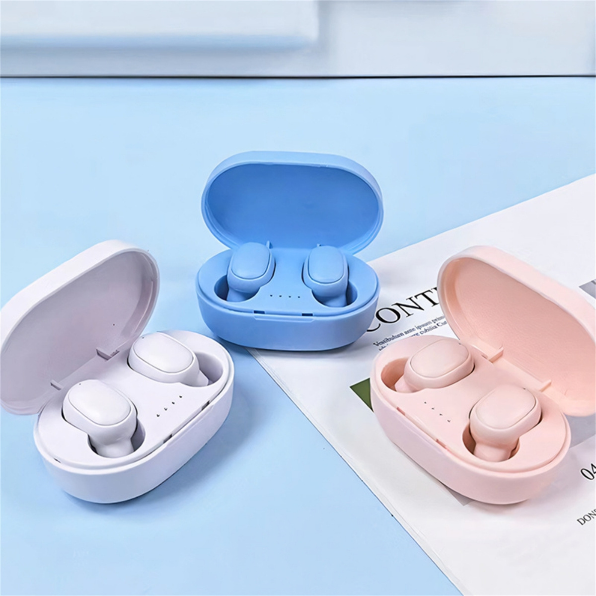 Drei bunte Ohrhörer in Ladeetuis. Blaue, rosa und weiße Etuis.