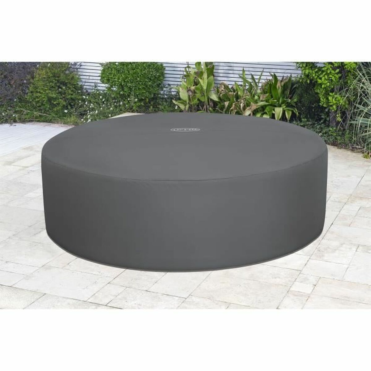 Graue Whirlpoolabdeckung auf gefliester Terrasse mit Pflanzen im Hintergrund.
