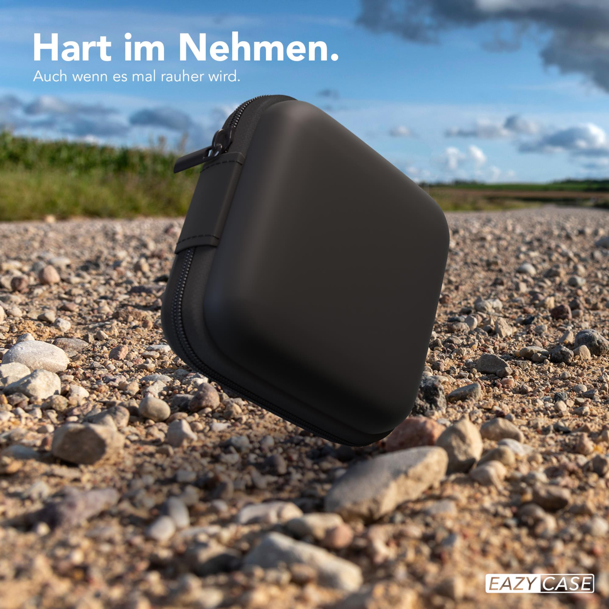Ein schwarzes quadratisches Etui auf einer Schotterstraße, mit blauem Himmel und Wolken.