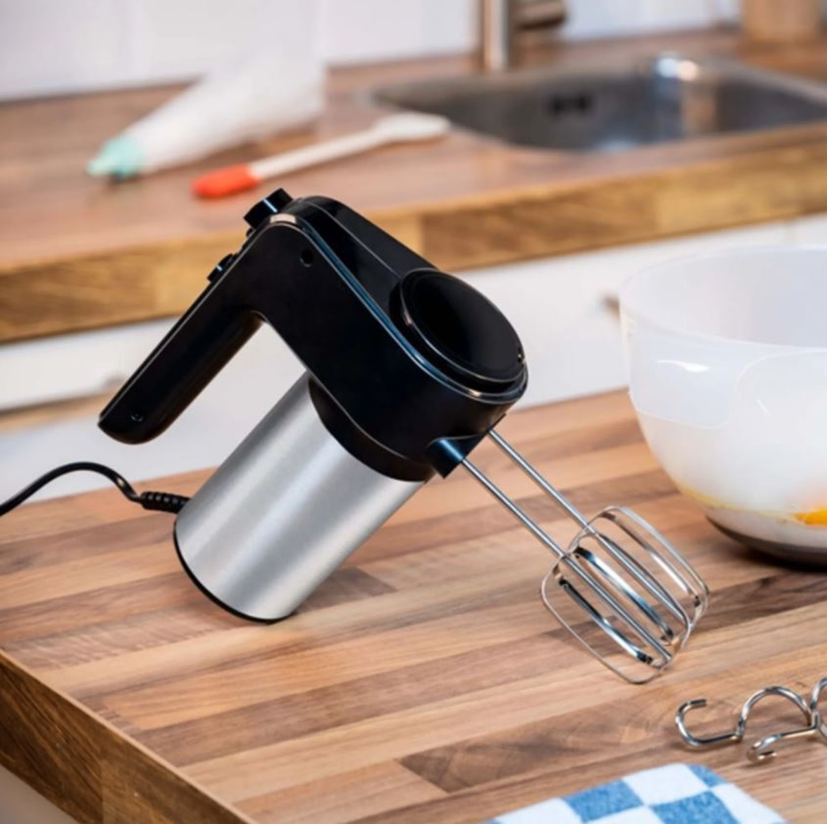 Schwarzer und silberner Handmixer mit einer Schüssel und anderen Kochutensilien.