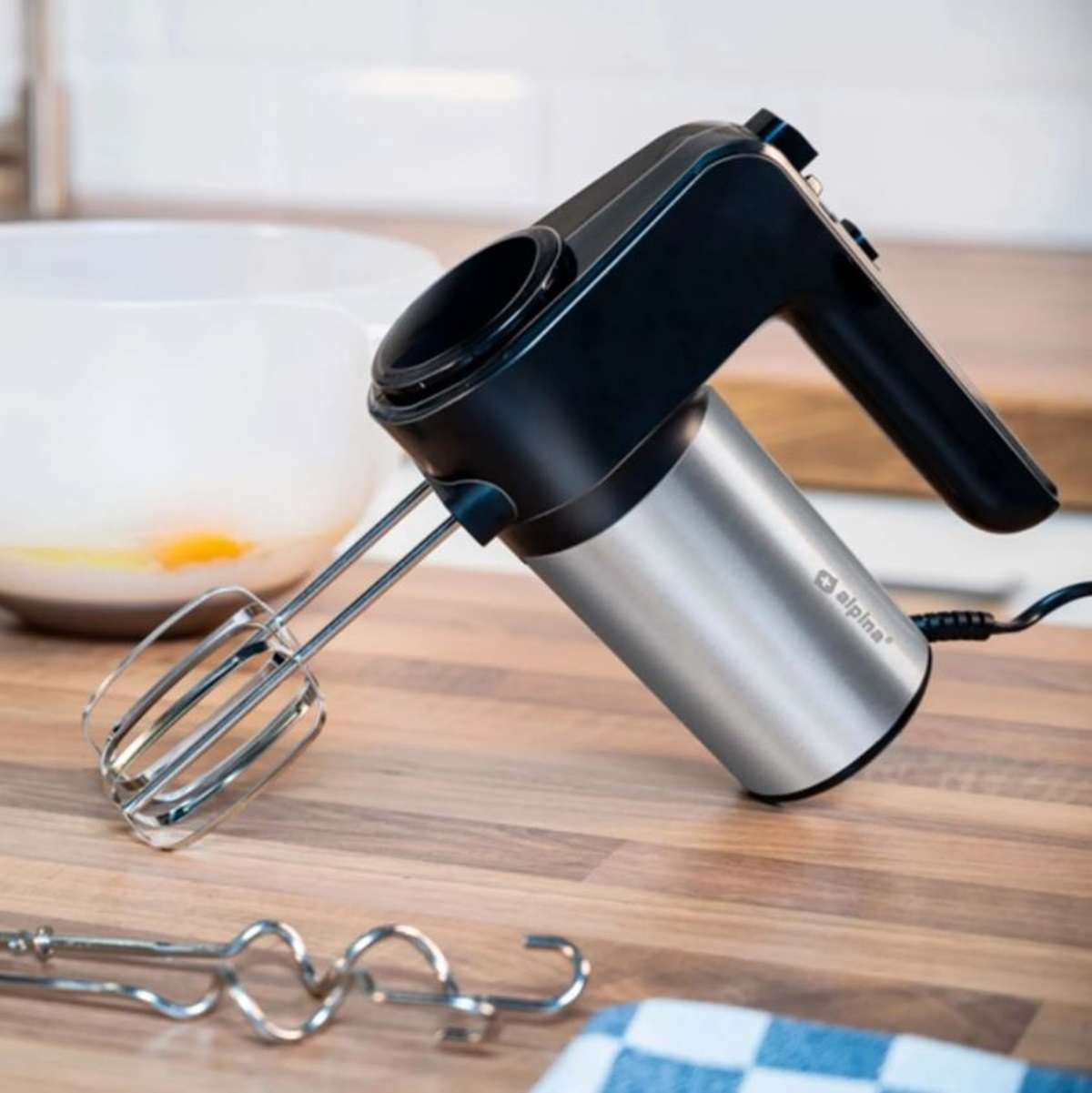 Handmixer auf Holzoberfläche mit Schüssel und zusätzlichem Rührwerkzeug in Sicht.