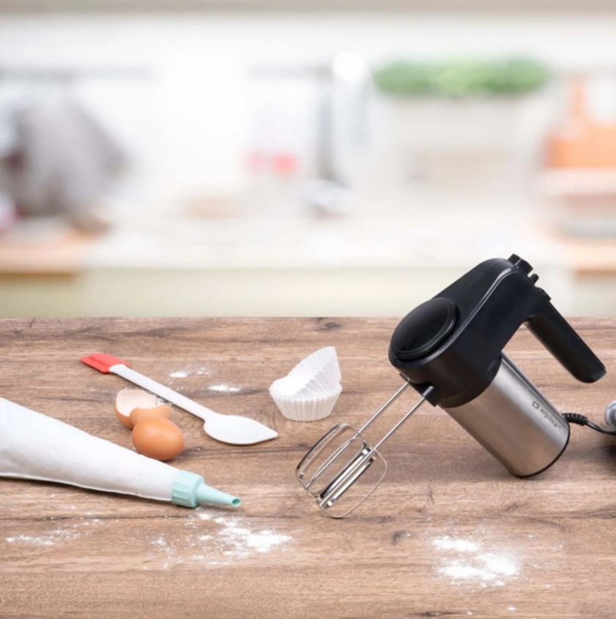 Ein Mixer mit Zubehör auf einem Holztisch, mit verschwommenem Küchenhintergrund.