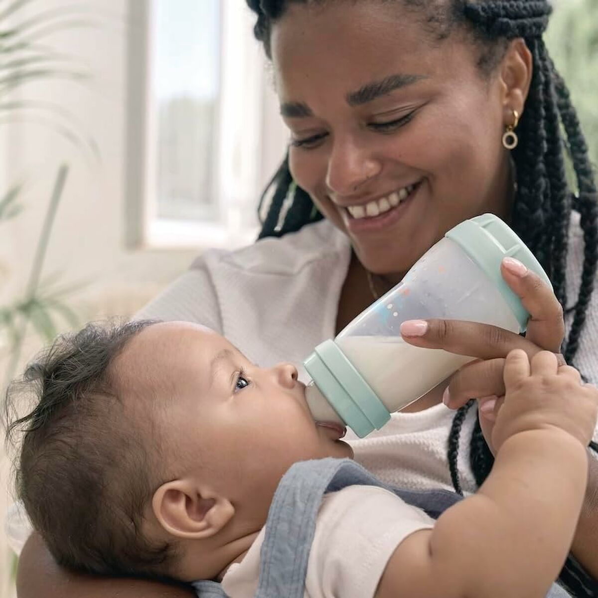 Eine Frau füttert ein Baby mit einer Flasche. Beide lächeln.