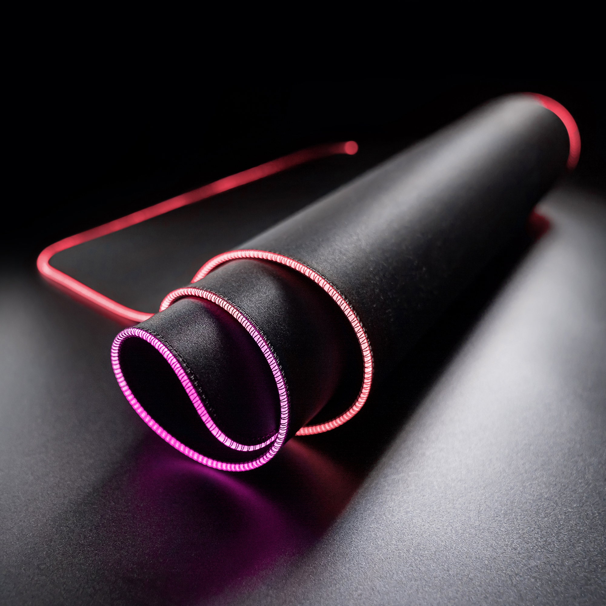 Czarna podkładka pod mysz z rolowanym wzorem i różowymi krawędziami LED na ciemnej powierzchni.