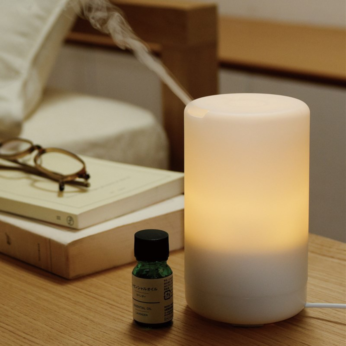 Weißer und beiger Diffusor für ätherische Öle. Eine kleine Ölflasche und eine Brille liegen auf dem Holztisch.