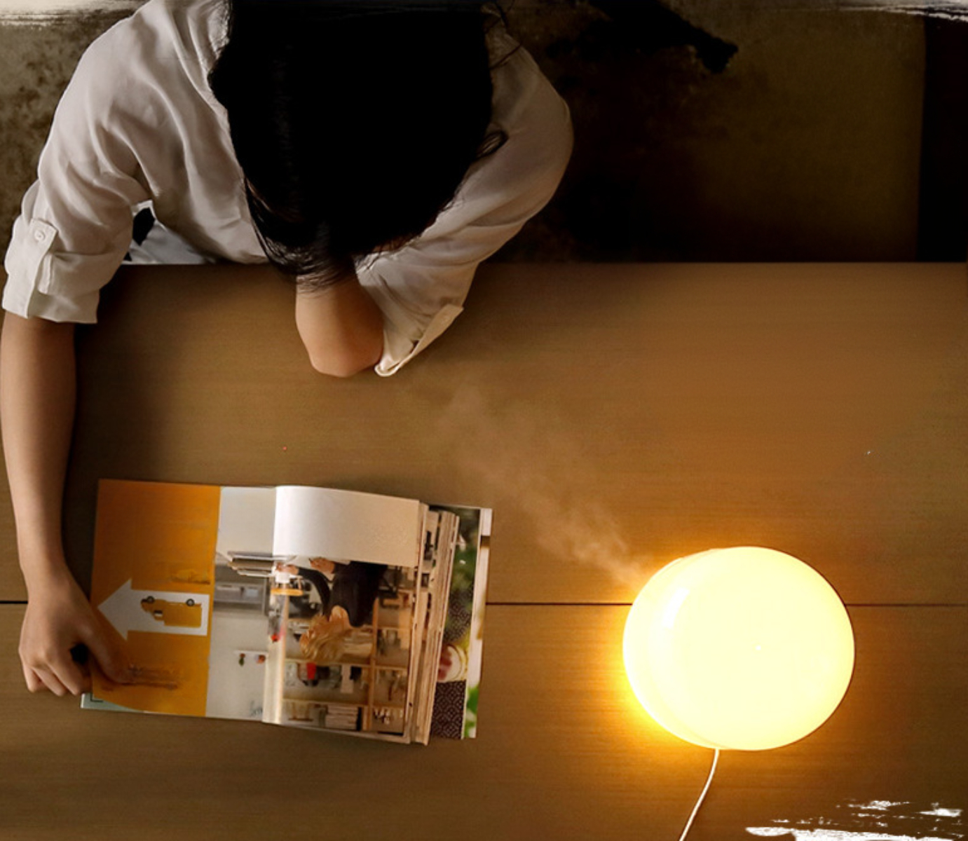 Eine Person liest eine Zeitschrift, eine leuchtende Lampe und ein Tisch. Die Lampe ist gelb und auf der rechten Seite.