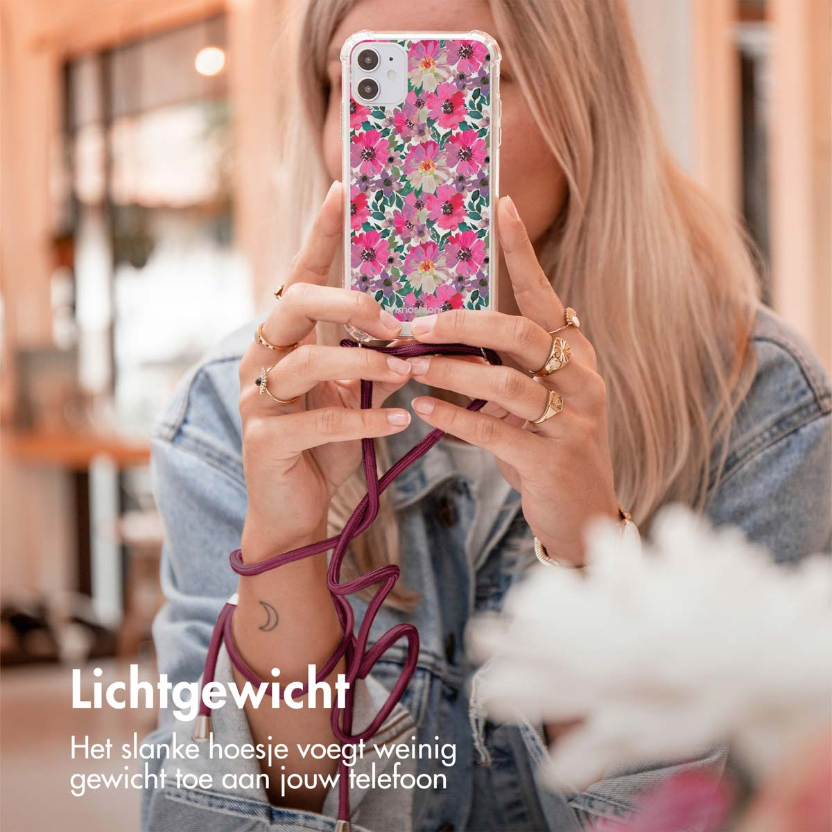 Une femme tenant un téléphone avec une coque florale, portant des bagues et une veste en jean.