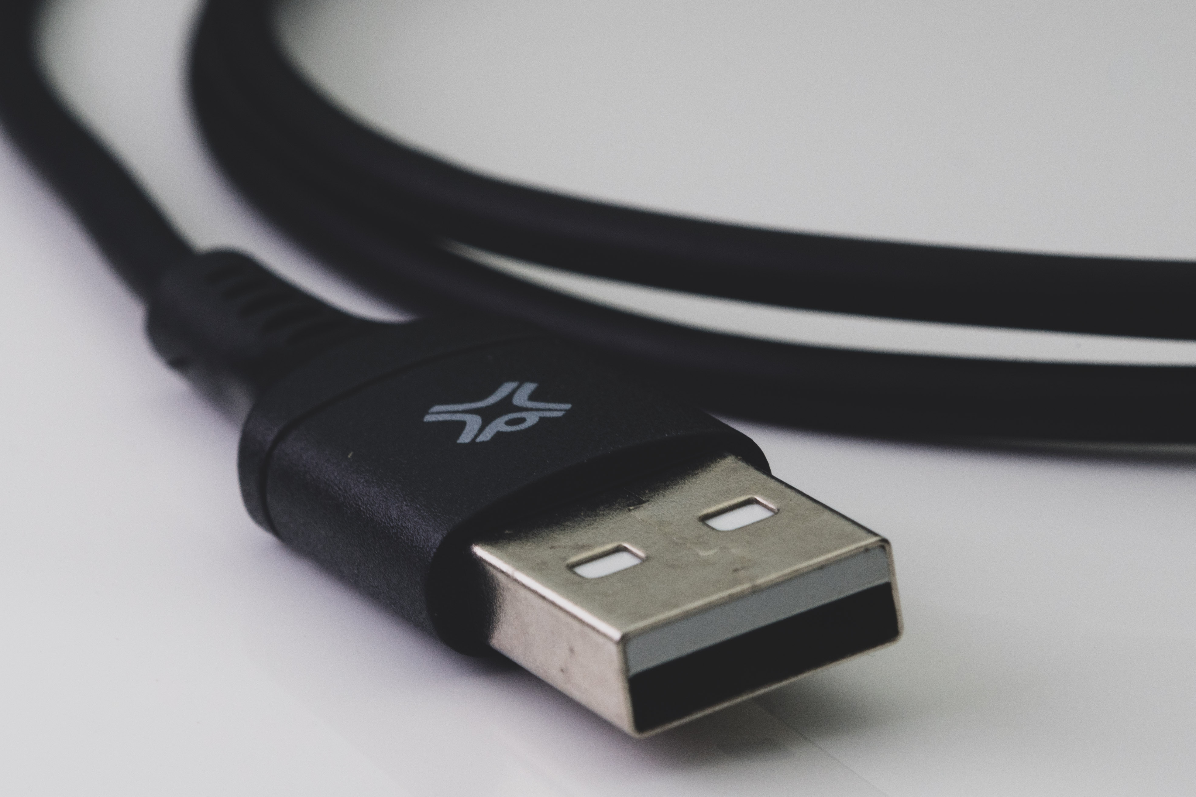 Close-up van een zwarte USB-kabel met een USB-connector. De kabel ligt op een wit oppervlak.