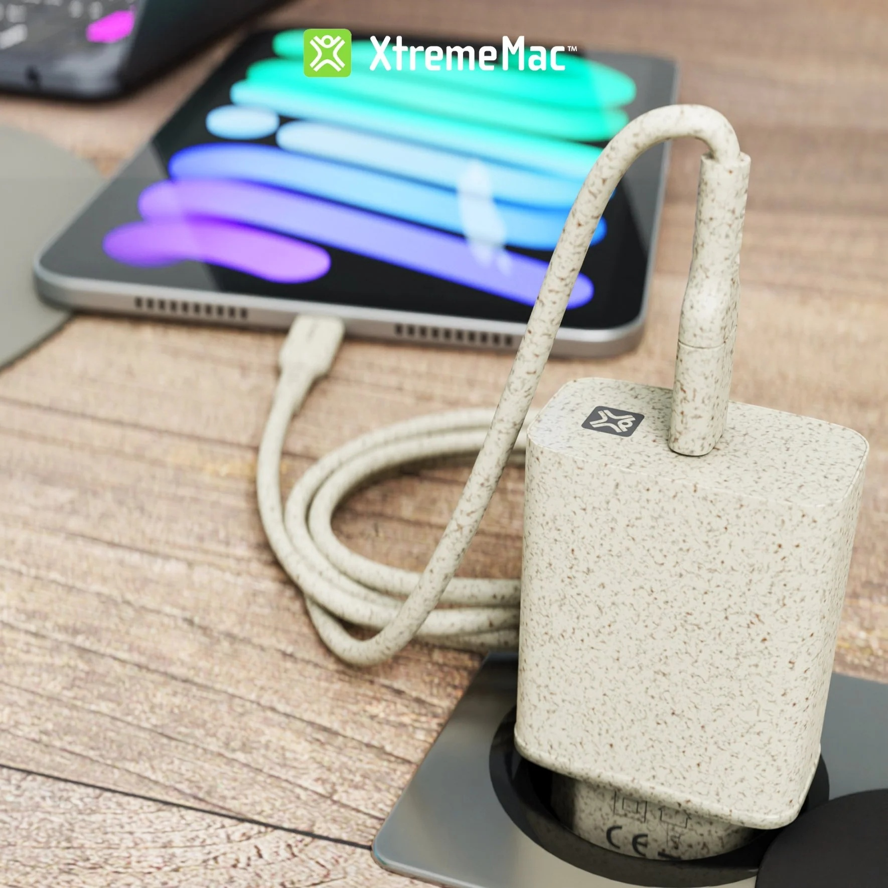 Witte en beige oplader met kabel in een stopcontact. Tablet op de achtergrond.