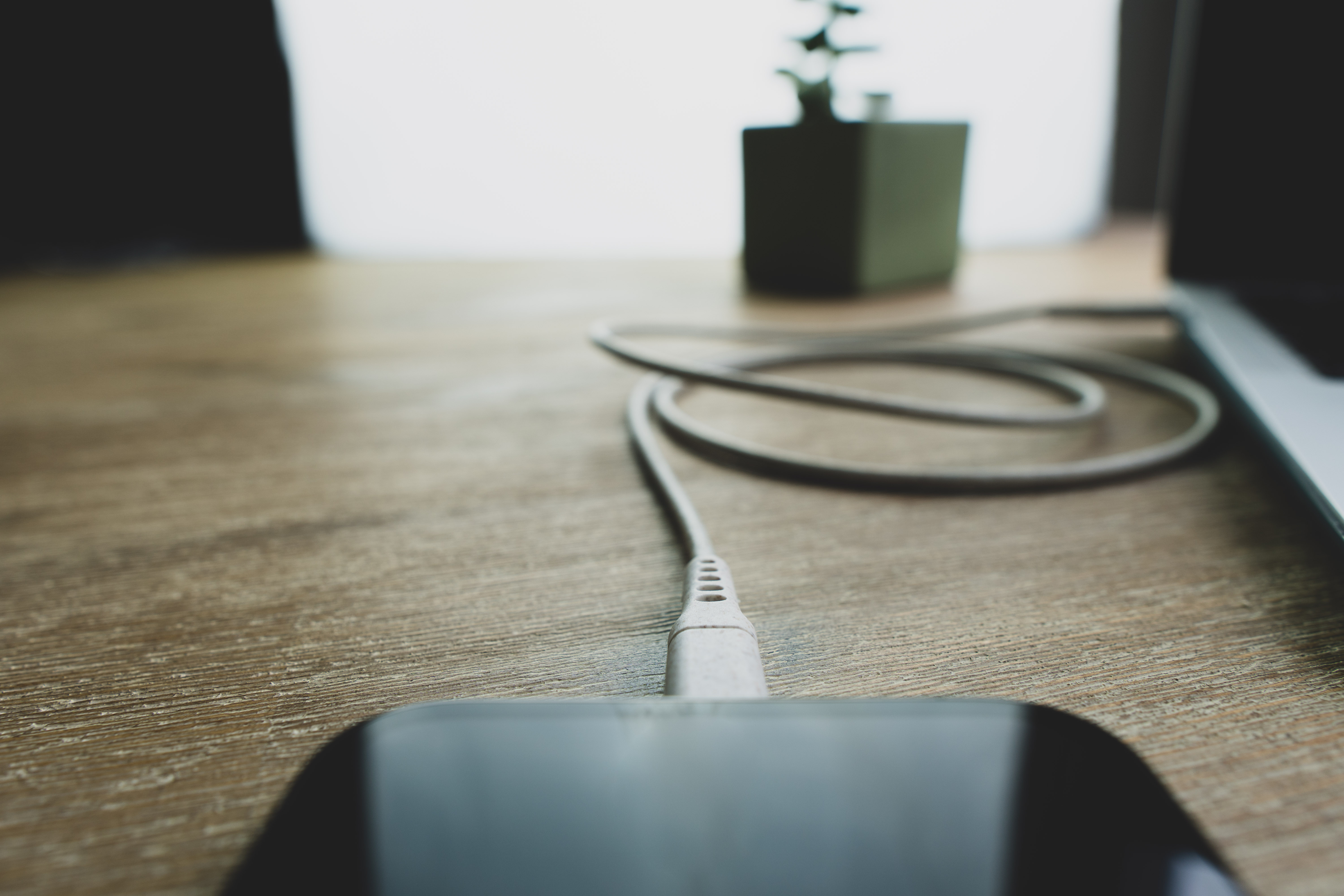 Een witte telefoon die oplaadt op een houten tafel, met een kleine plant op de achtergrond.