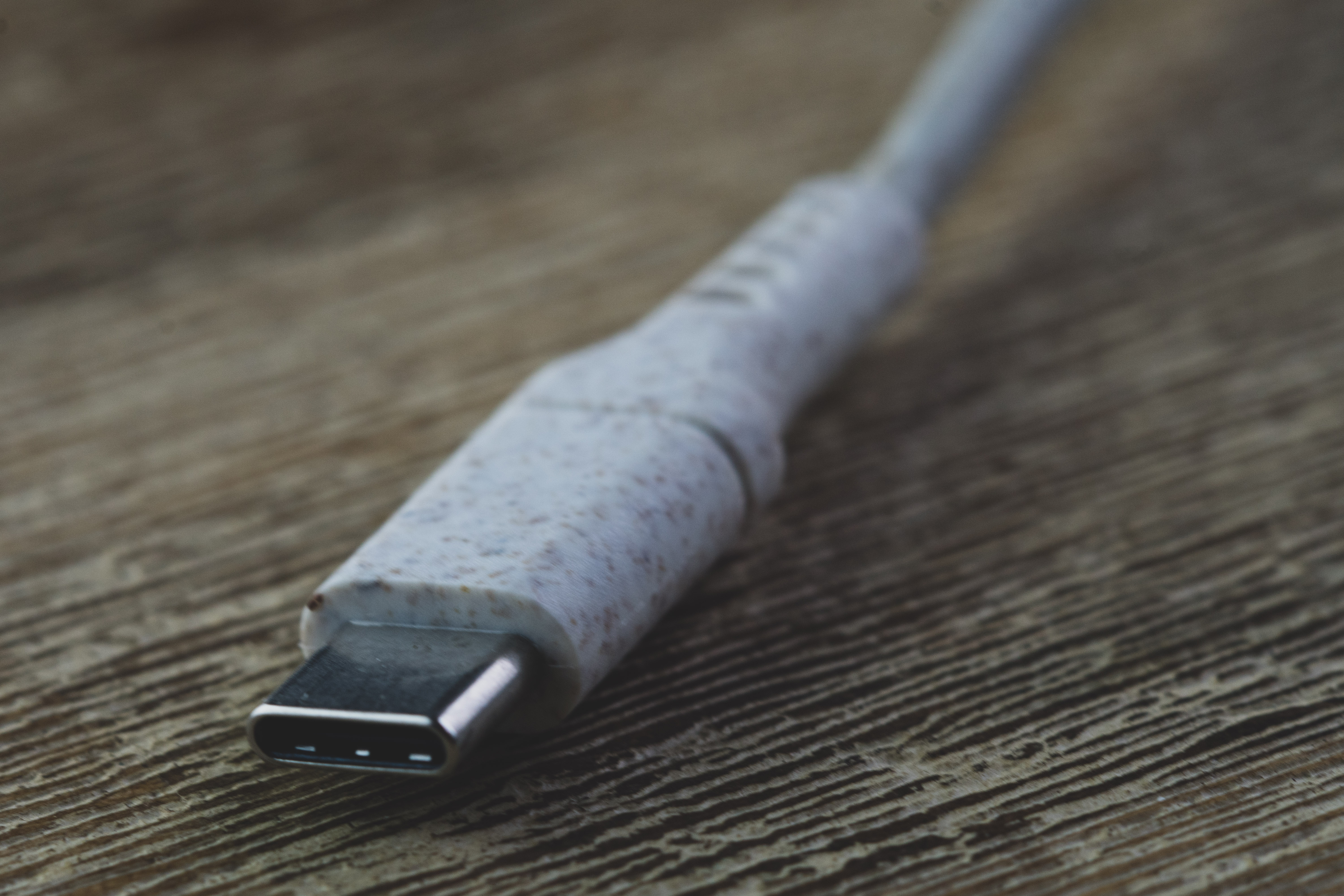 Close-up van een USB-C-kabeluiteinde tegen een achtergrond met houtnerf. De kabel is wit met spikkels.