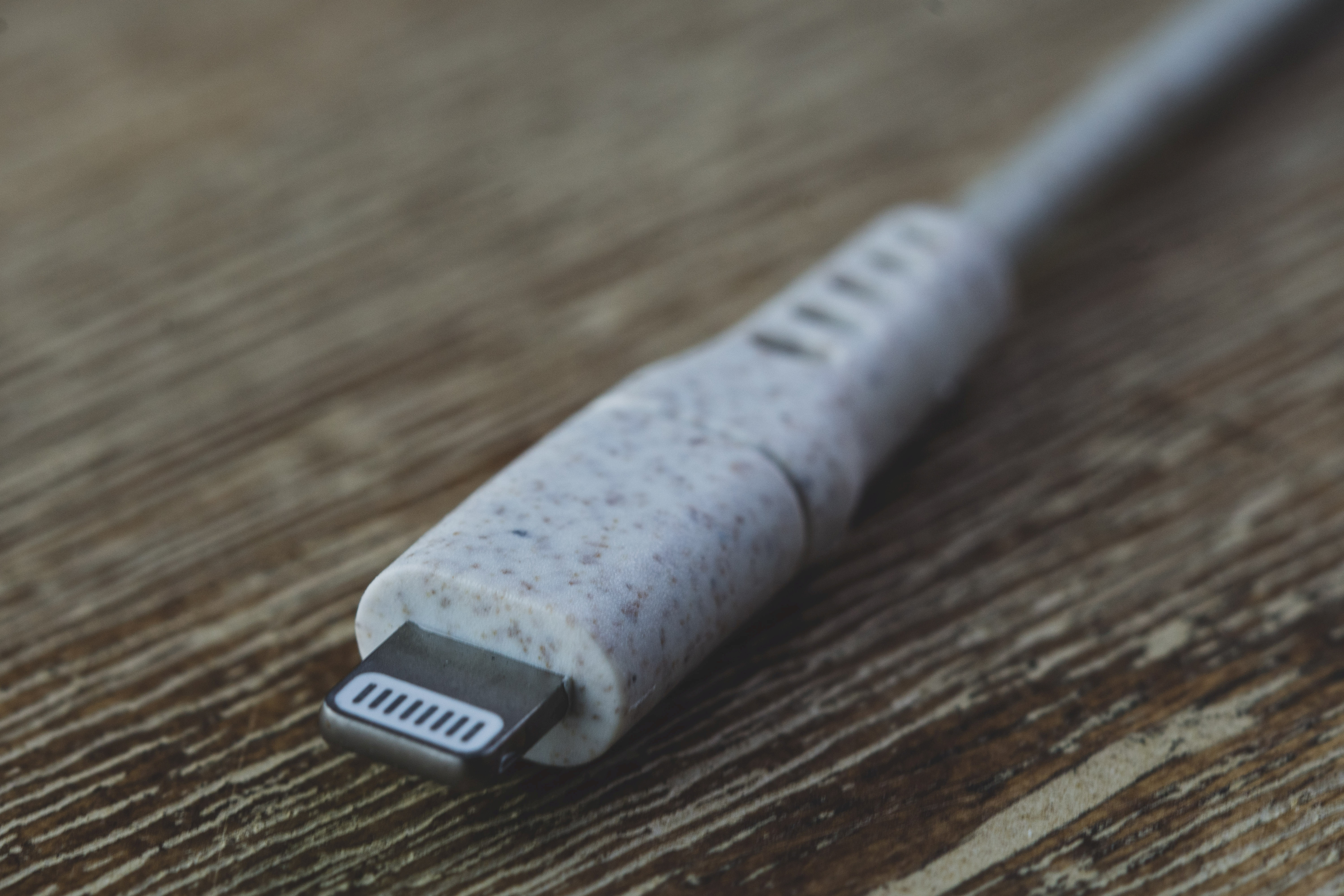 Close-up van een witte en gespikkelde Lightning-connector tegen een achtergrond met houtnerf.