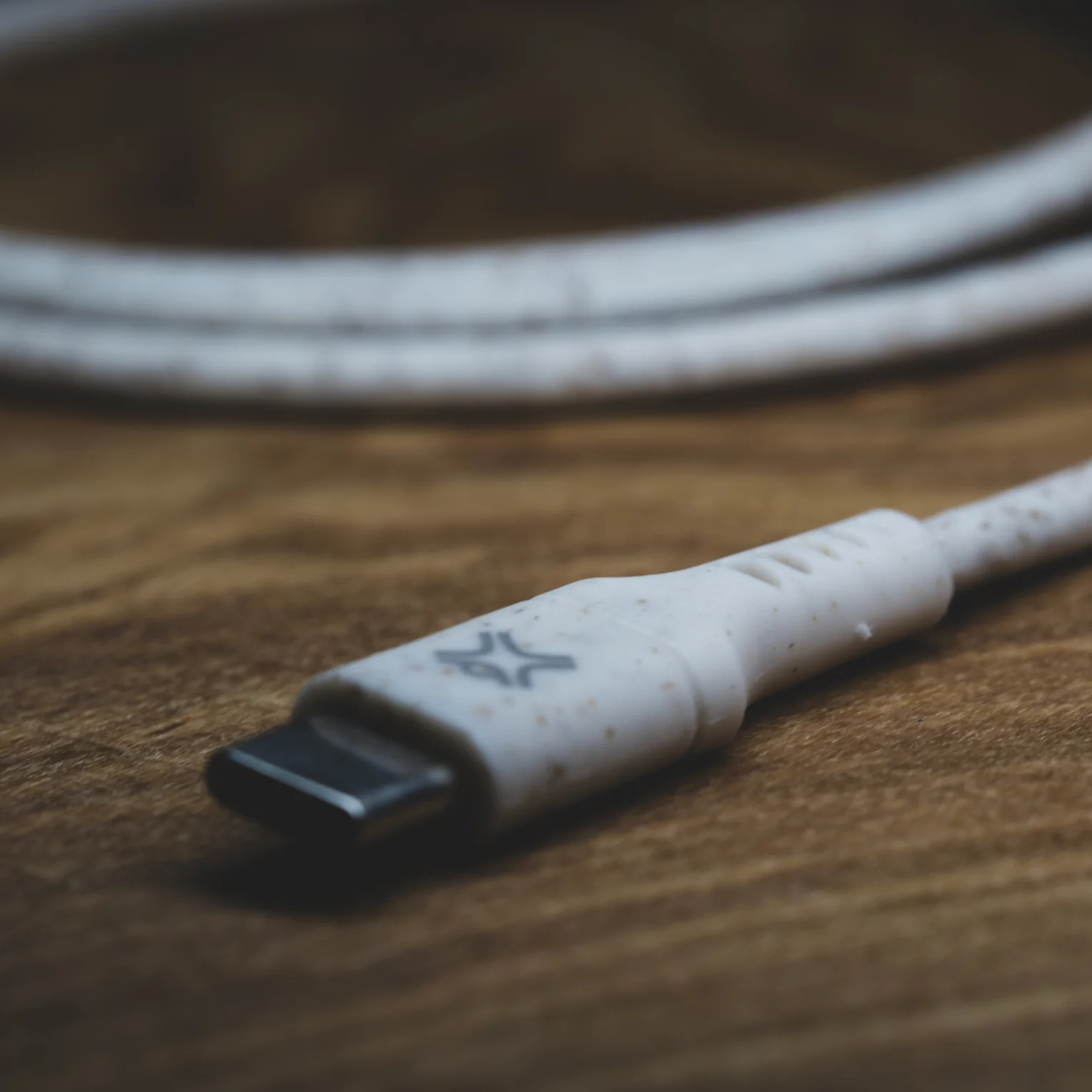 Close-up van een witte kabel met een USB-C connector. De kabel ligt op een houten oppervlak.