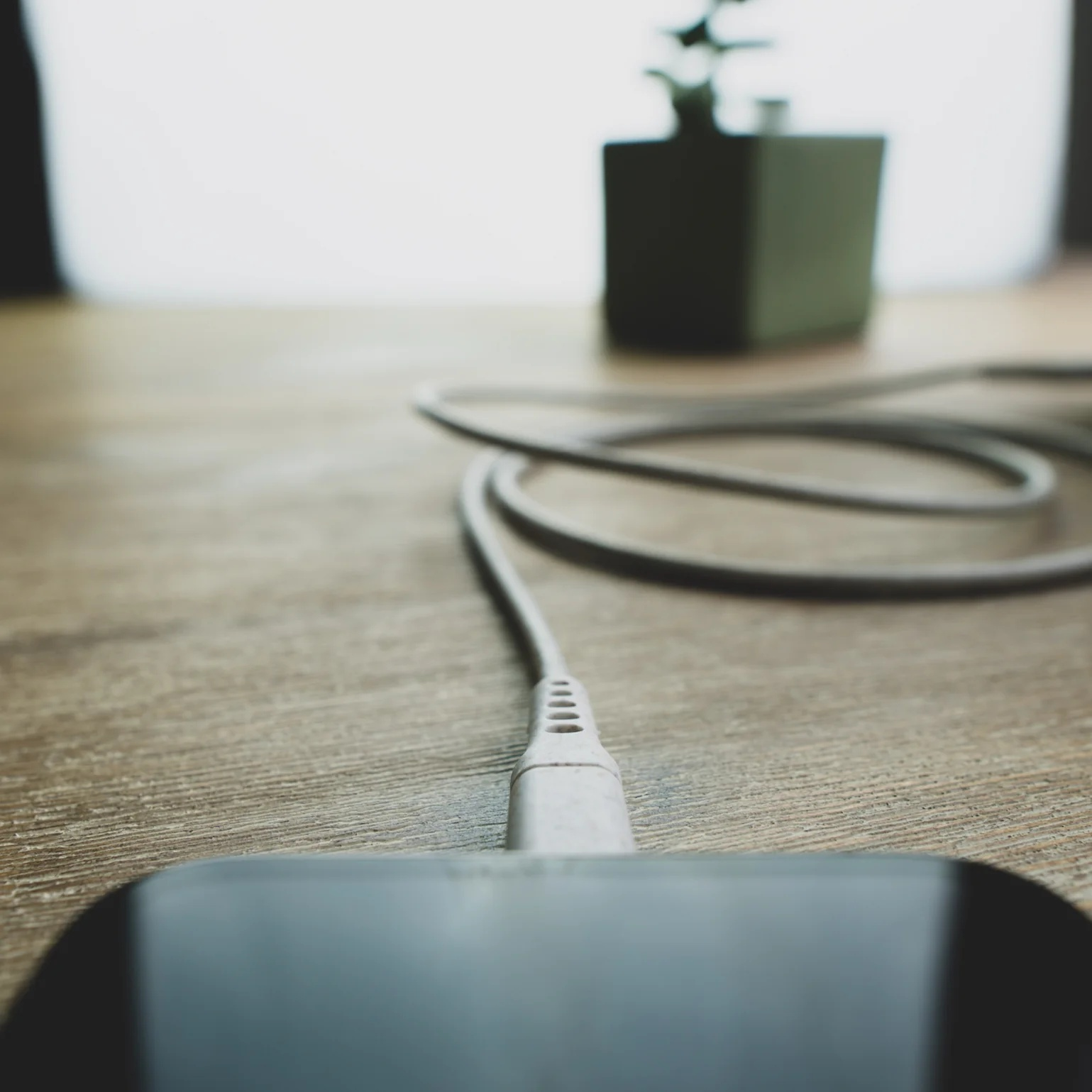 Close-up van een telefoon die oplaadt. Een witte kabel is aangesloten op de telefoon. Een groene doos op de achtergrond.
