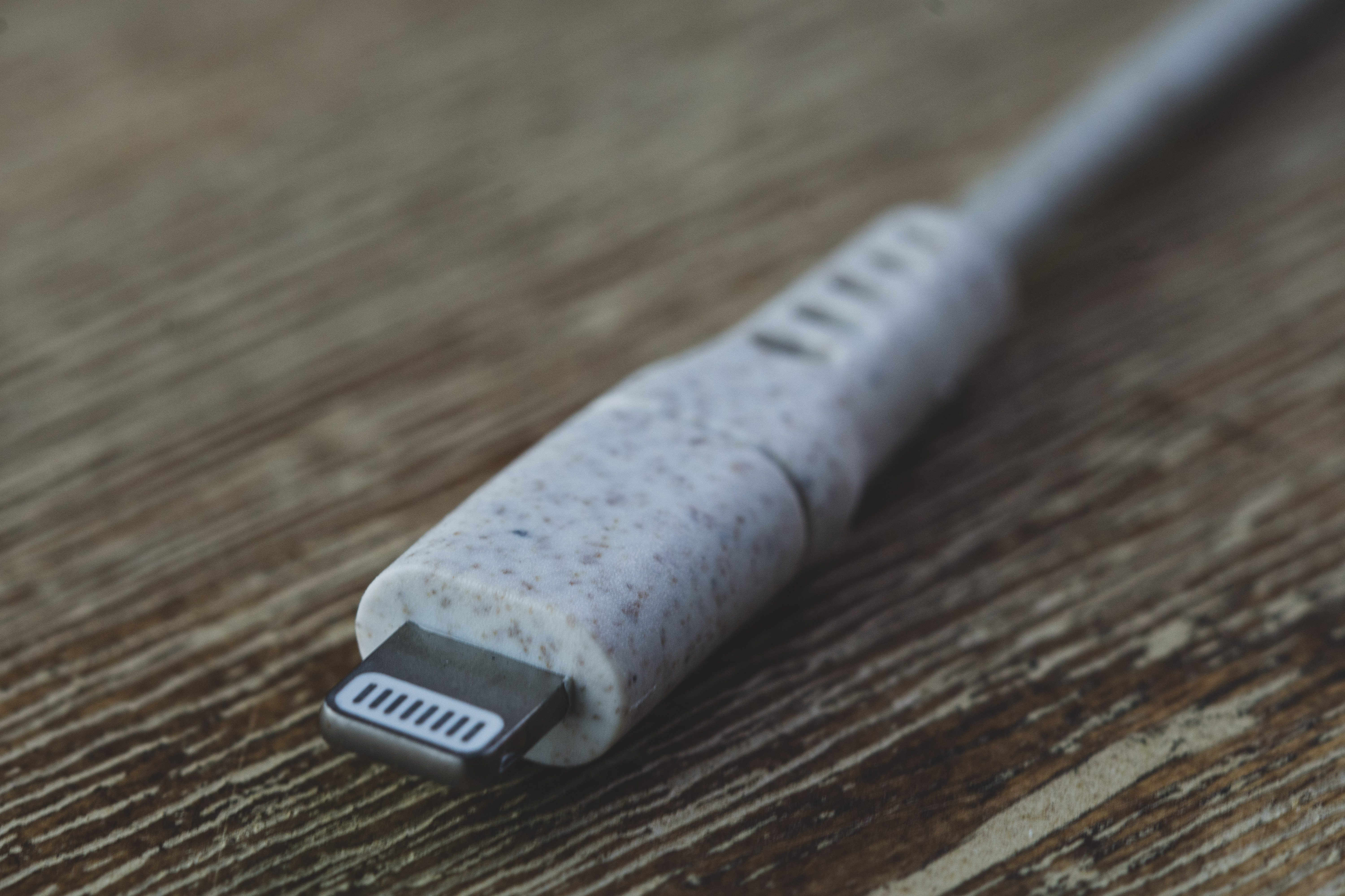 Close-up van een iPhone lightning-kabel. De connector is zilverkleurig met een gespikkelde witte en grijze kabel.