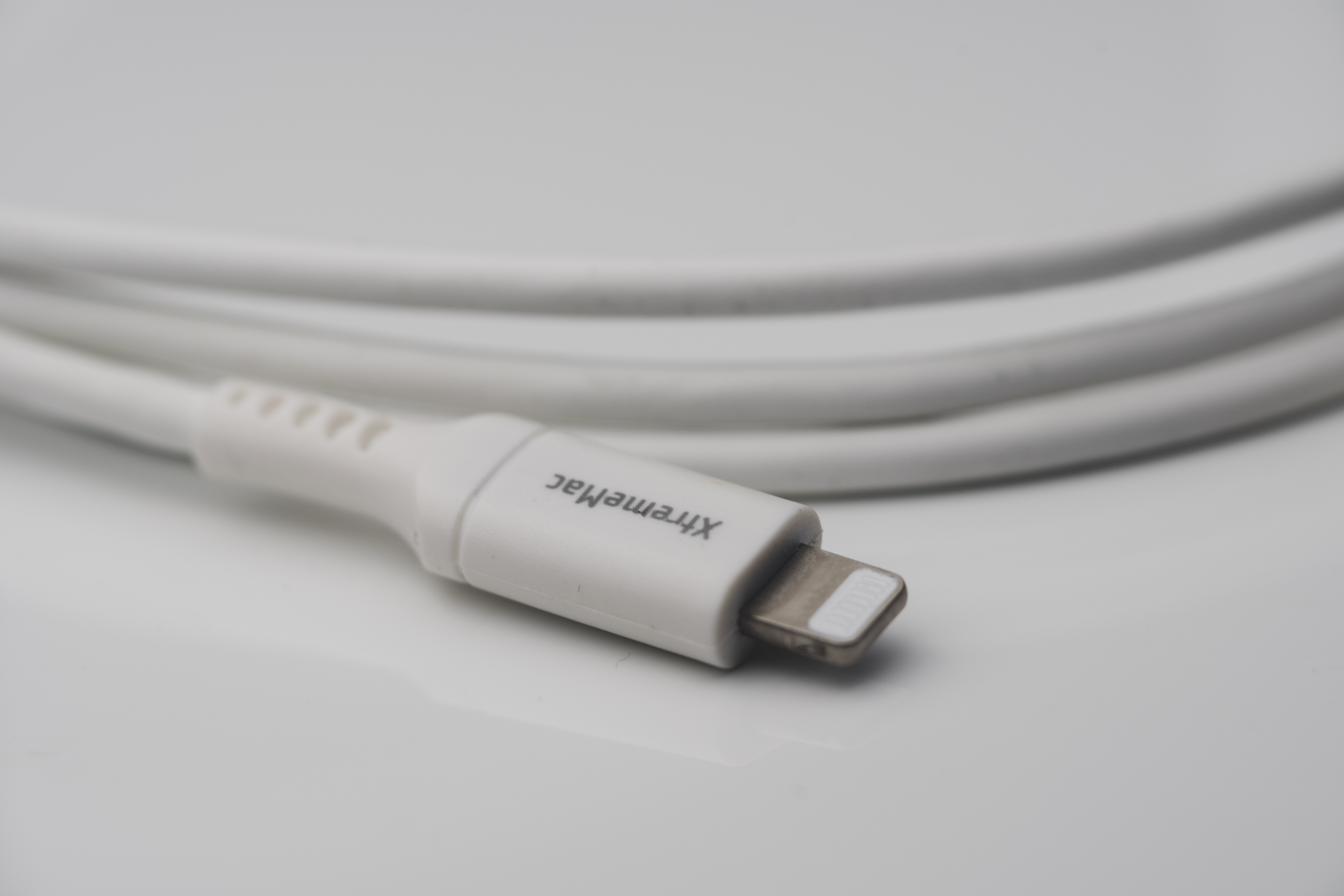 Witte kabel met een Lightning-connector, gemarkeerd met "XtremeMac", liggend op een wit oppervlak. De kabel is opgerold.