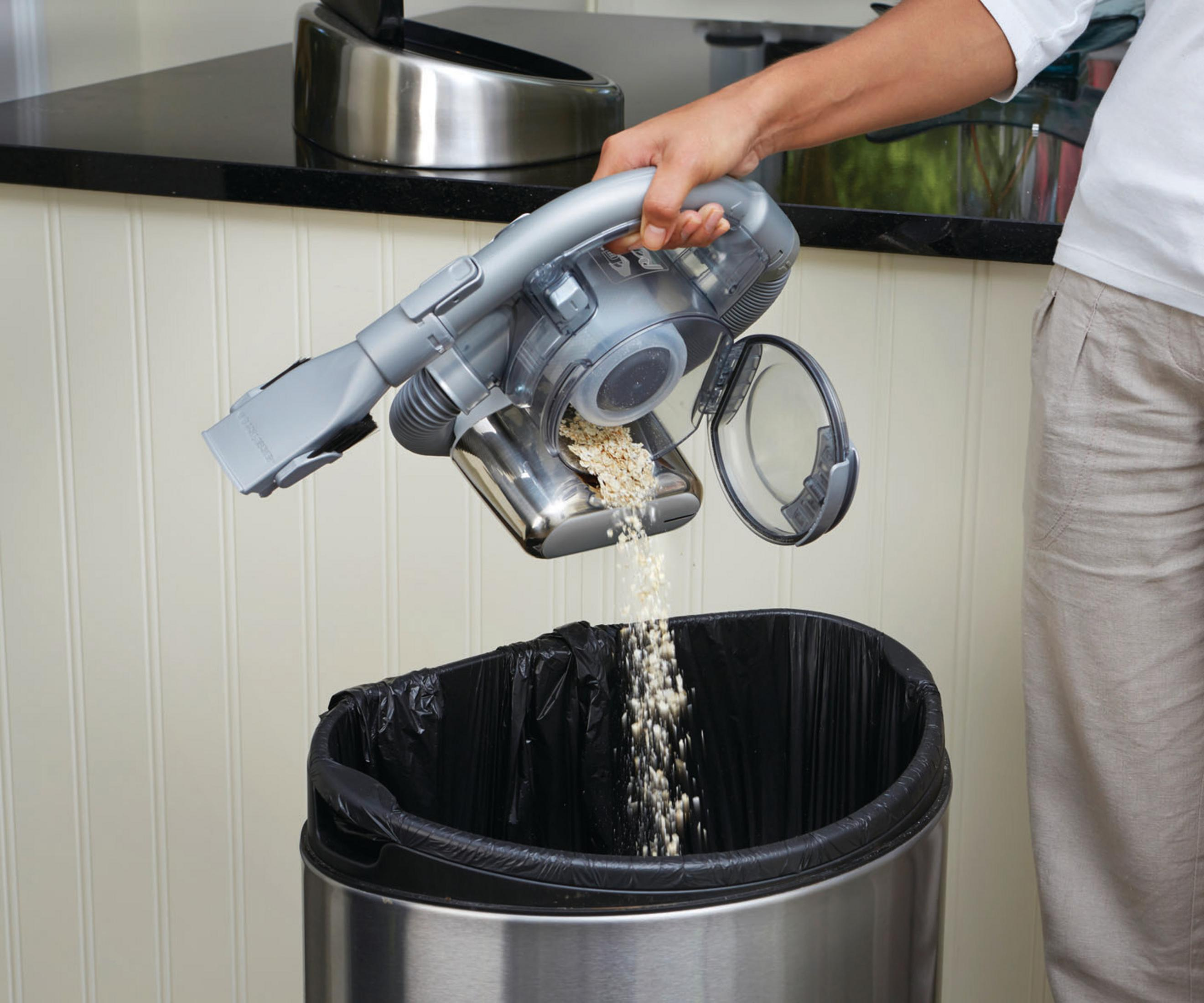 Osoba opróżnia odkurzacz do kosza na śmieci. Zawartość wpada do czarnego worka na śmieci.