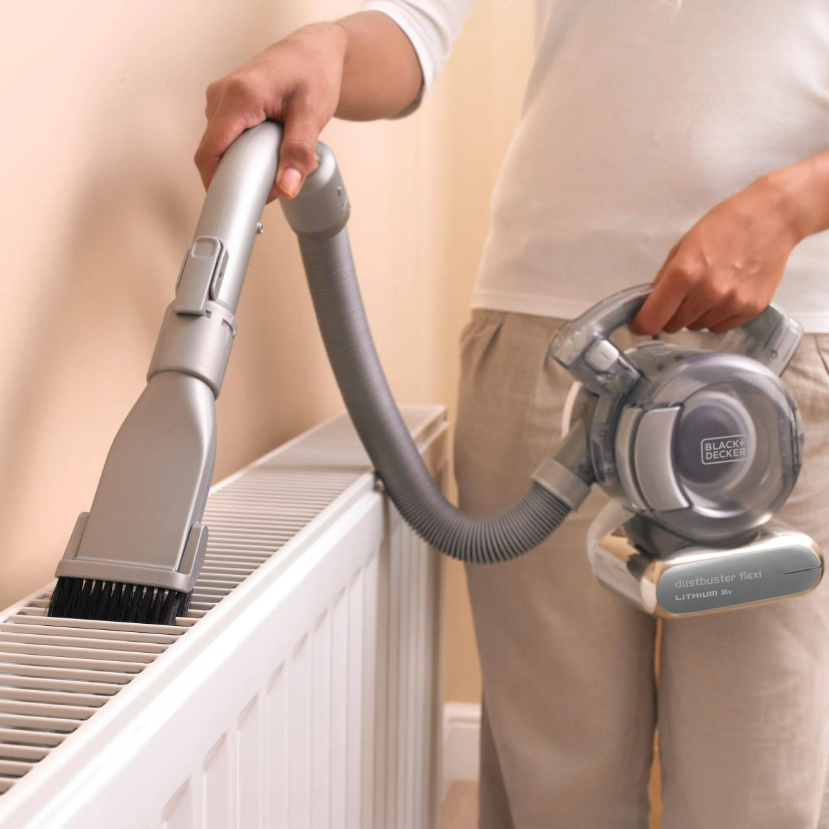 Osoba odkurzająca kaloryfer za pomocą odkurzacza ręcznego.