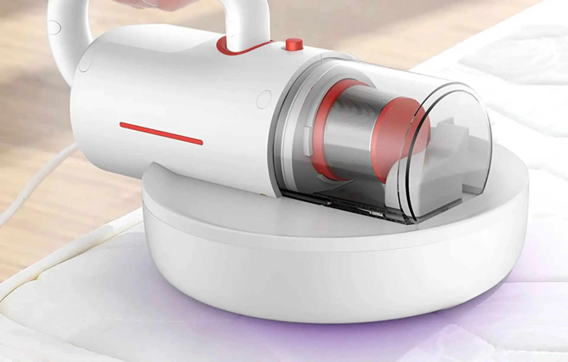 Biały odkurzacz ręczny z przezroczystym pojemnikiem na kurz, w użyciu na materacu.