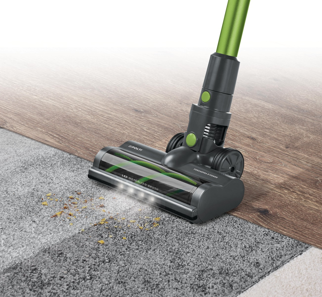 Una aspiradora limpiando una alfombra. La aspiradora es gris y verde.