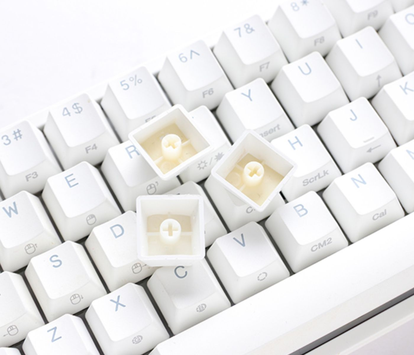 Primer plano de un teclado blanco con teclas quitadas, revelando los componentes internos de las teclas. El fondo es blanco.