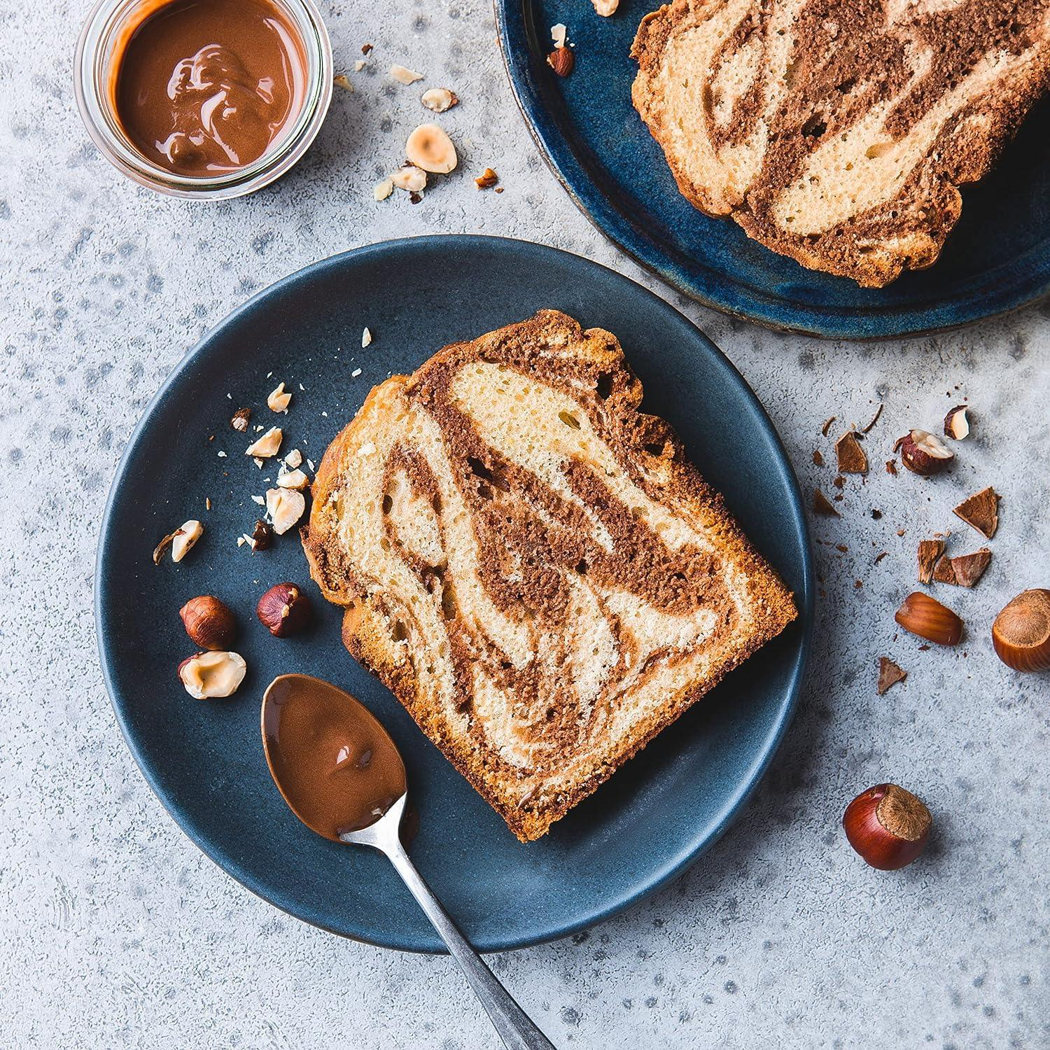 Une tranche de gâteau marbré avec des noisettes et de la sauce au chocolat sur une assiette bleue.