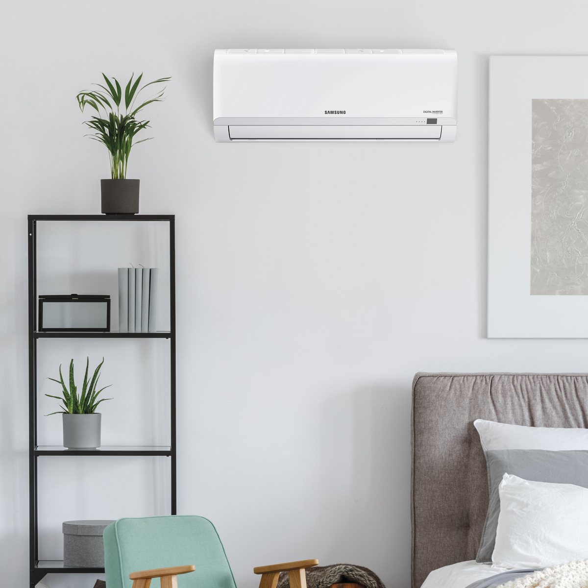 Un condizionatore Samsung bianco montato a parete. C'è una mensola con piante e decorazioni sotto, e un letto è visibile.