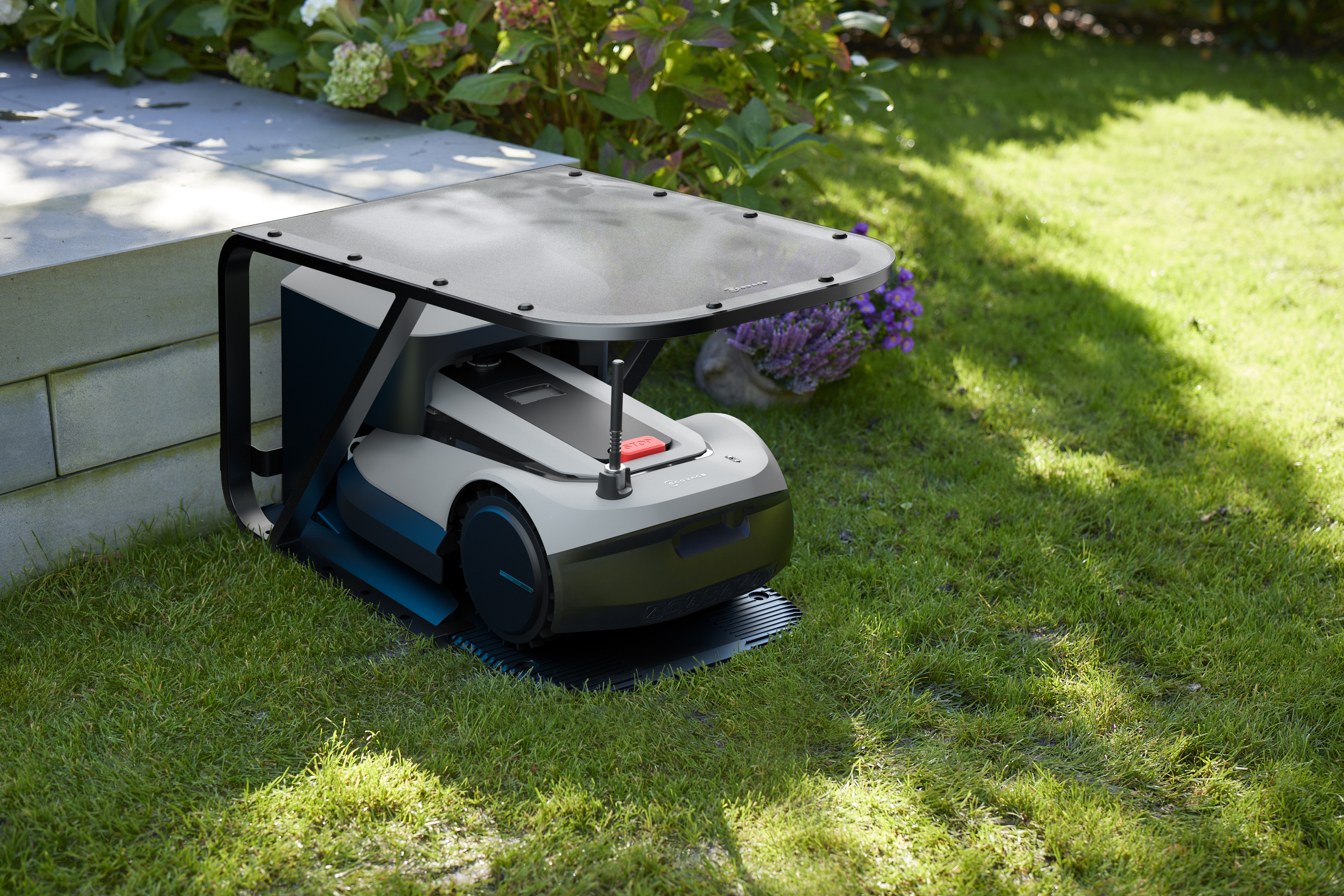 Ein Roboter-Rasenmäher in einer Garage mit schwarzem Dach. Der Rasenmäher steht auf einem grünen Rasen.