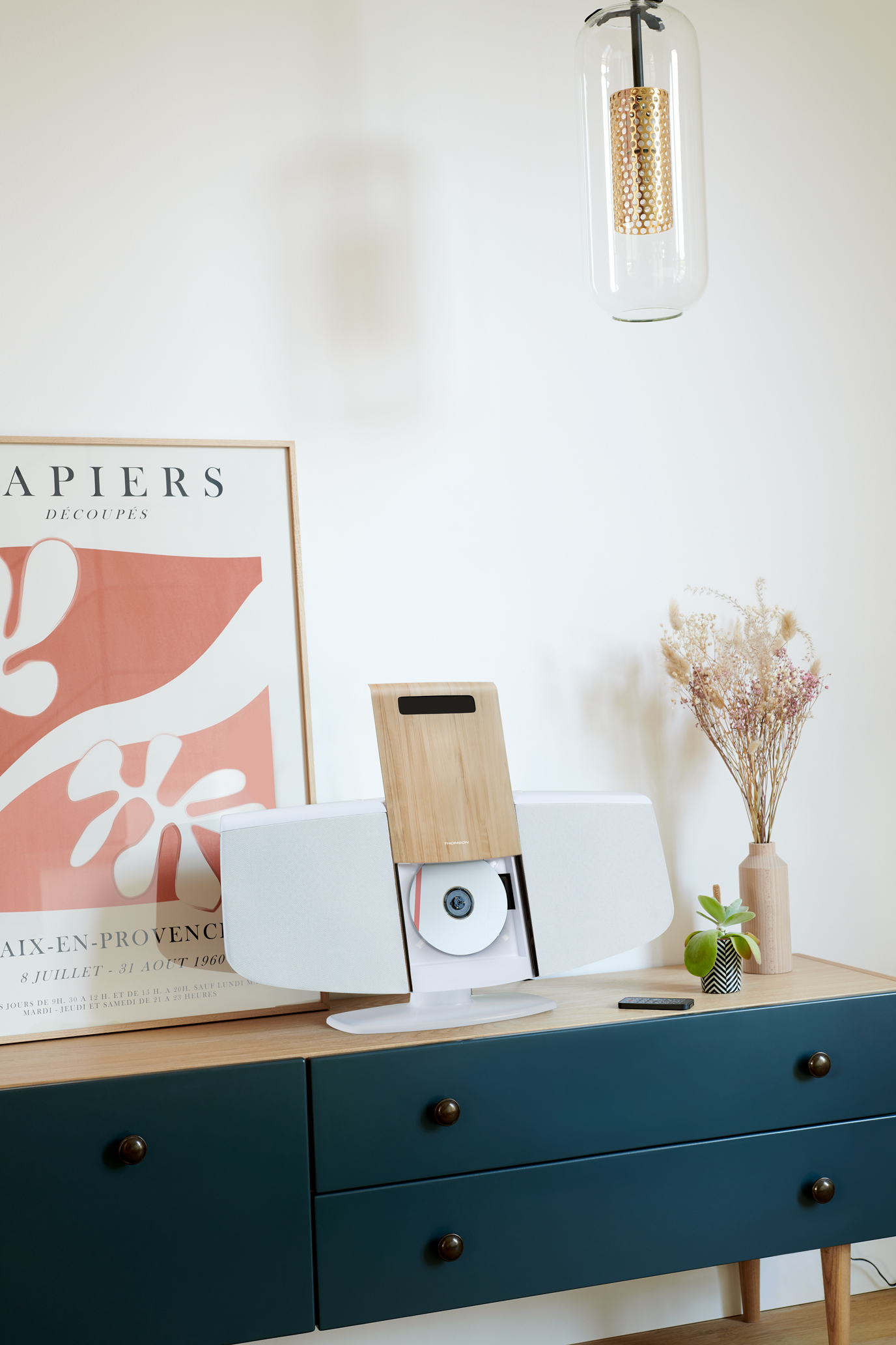 Zestaw stereo na niebieskiej szafce z plakatem i wazonem. Lampa nad głową.