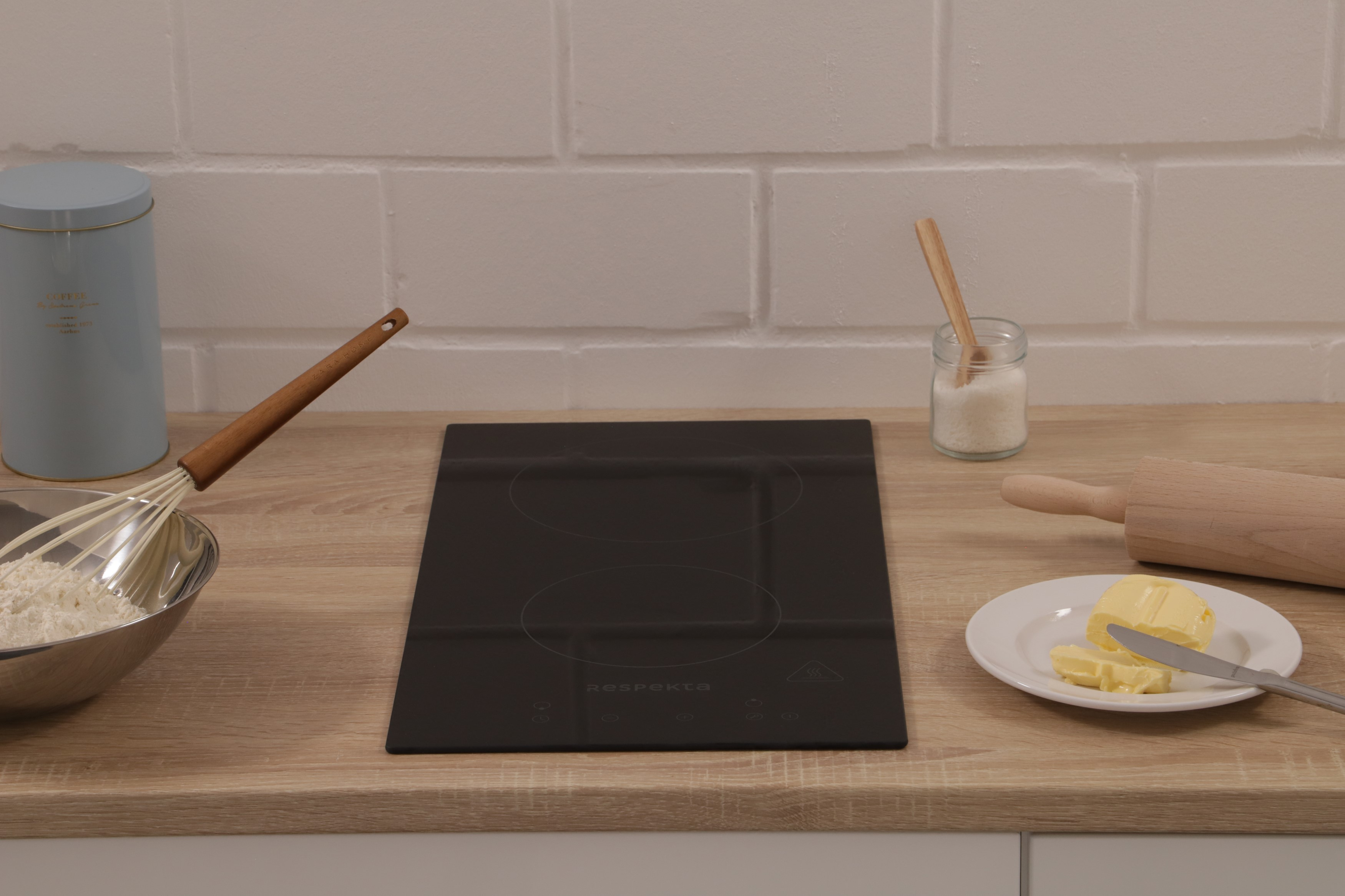 Kitchen counter with cooking utensils. Includes a hob, whisk, flour, and butter.