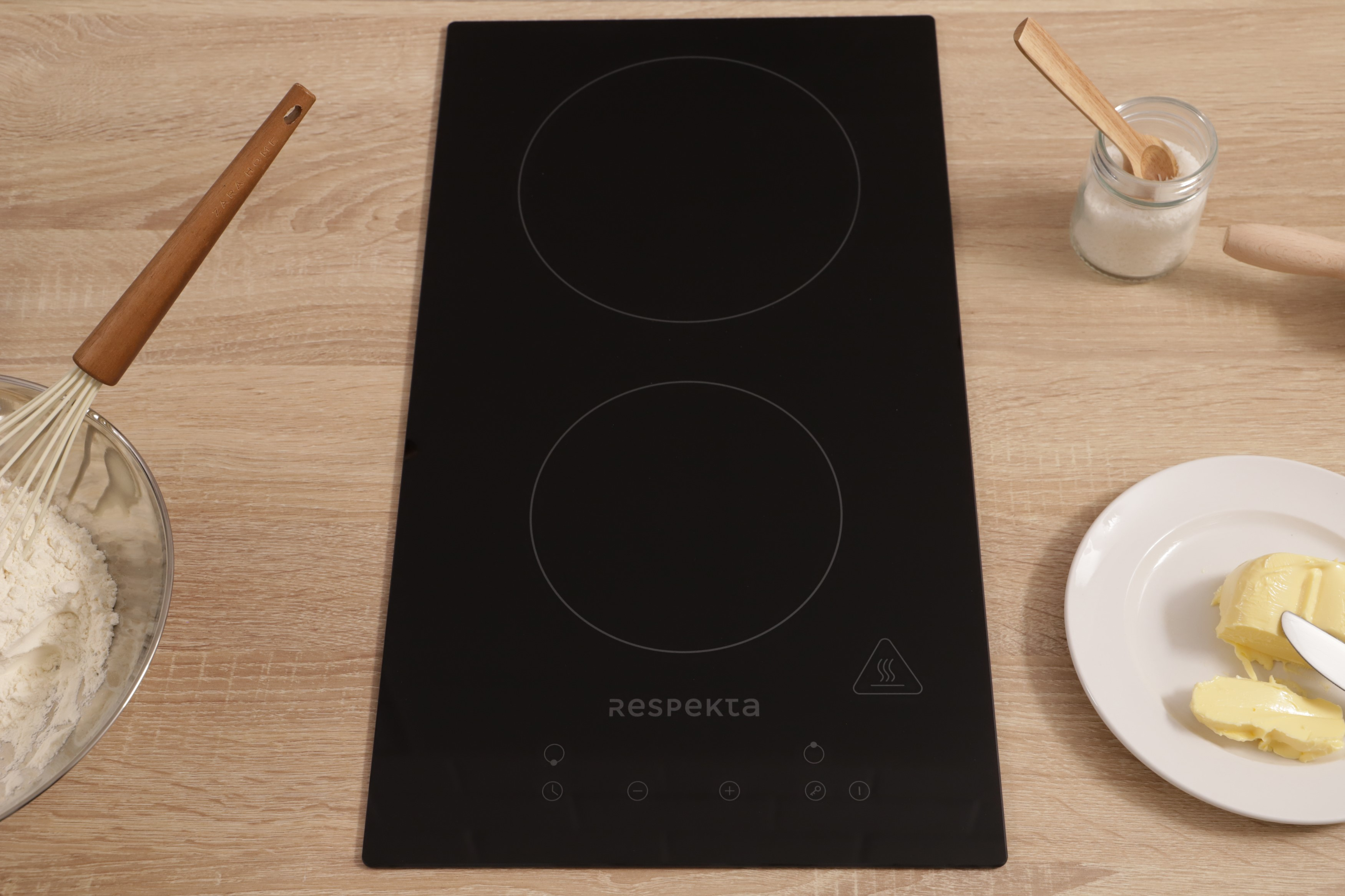 Black electric cooktop with two burners and kitchen utensils around.