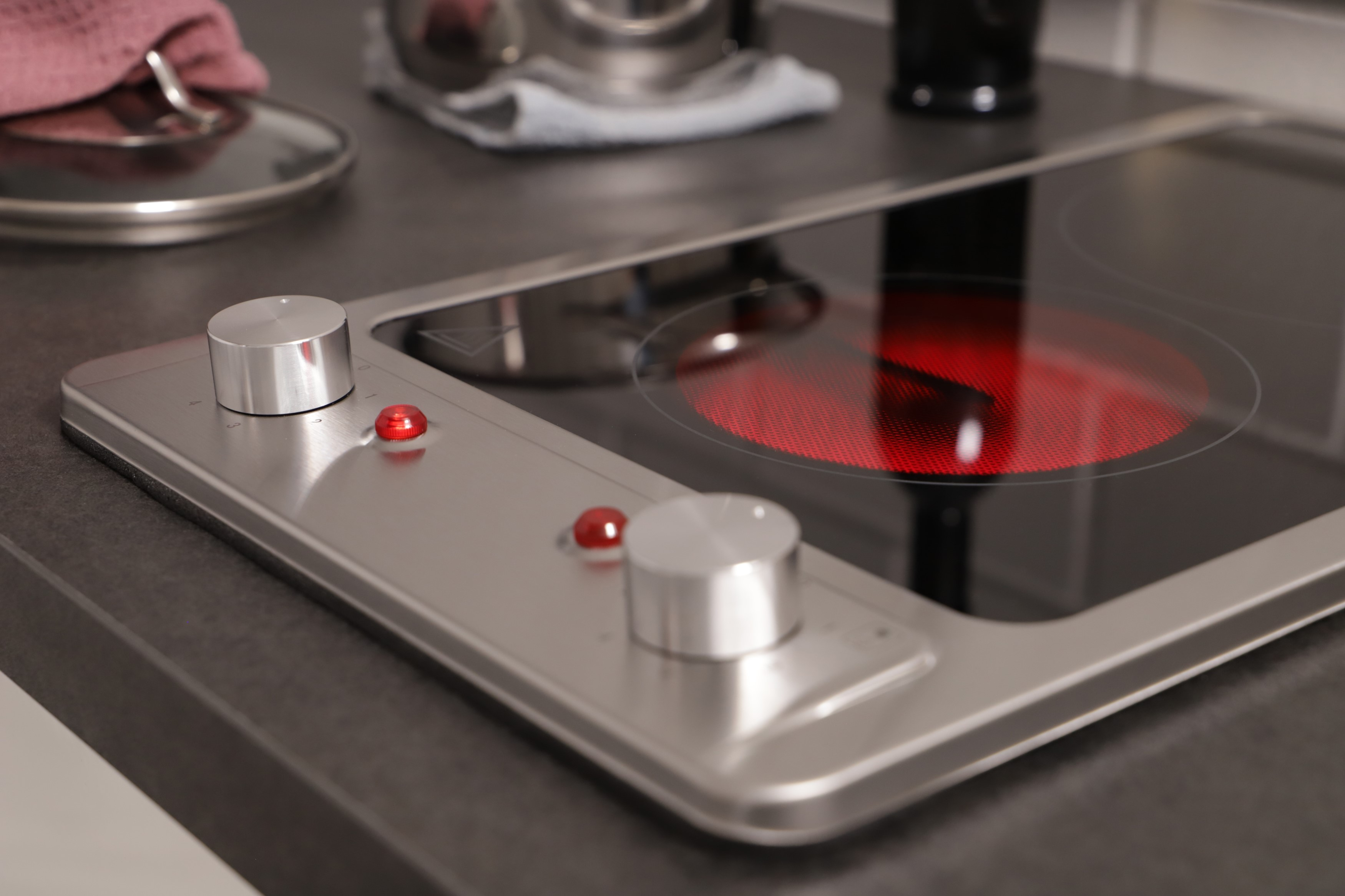 A stainless steel cooktop with two burners, one red and glowing. Knobs are on the left.