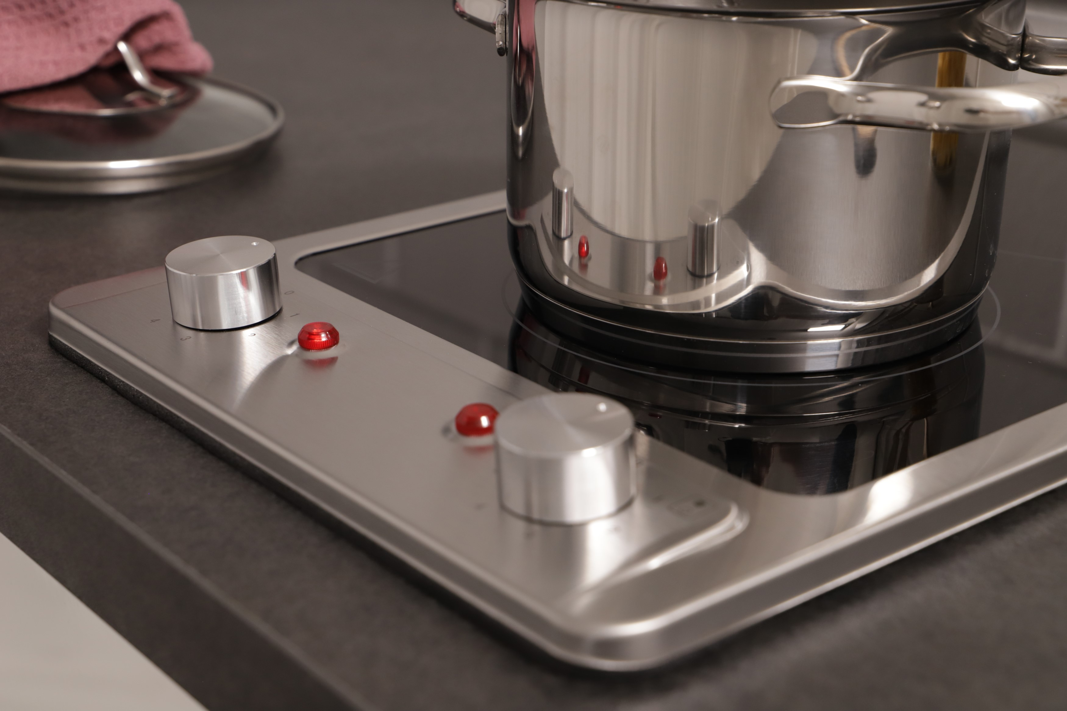 Close-up of a stovetop with a pot and controls, a red indicator is lit.