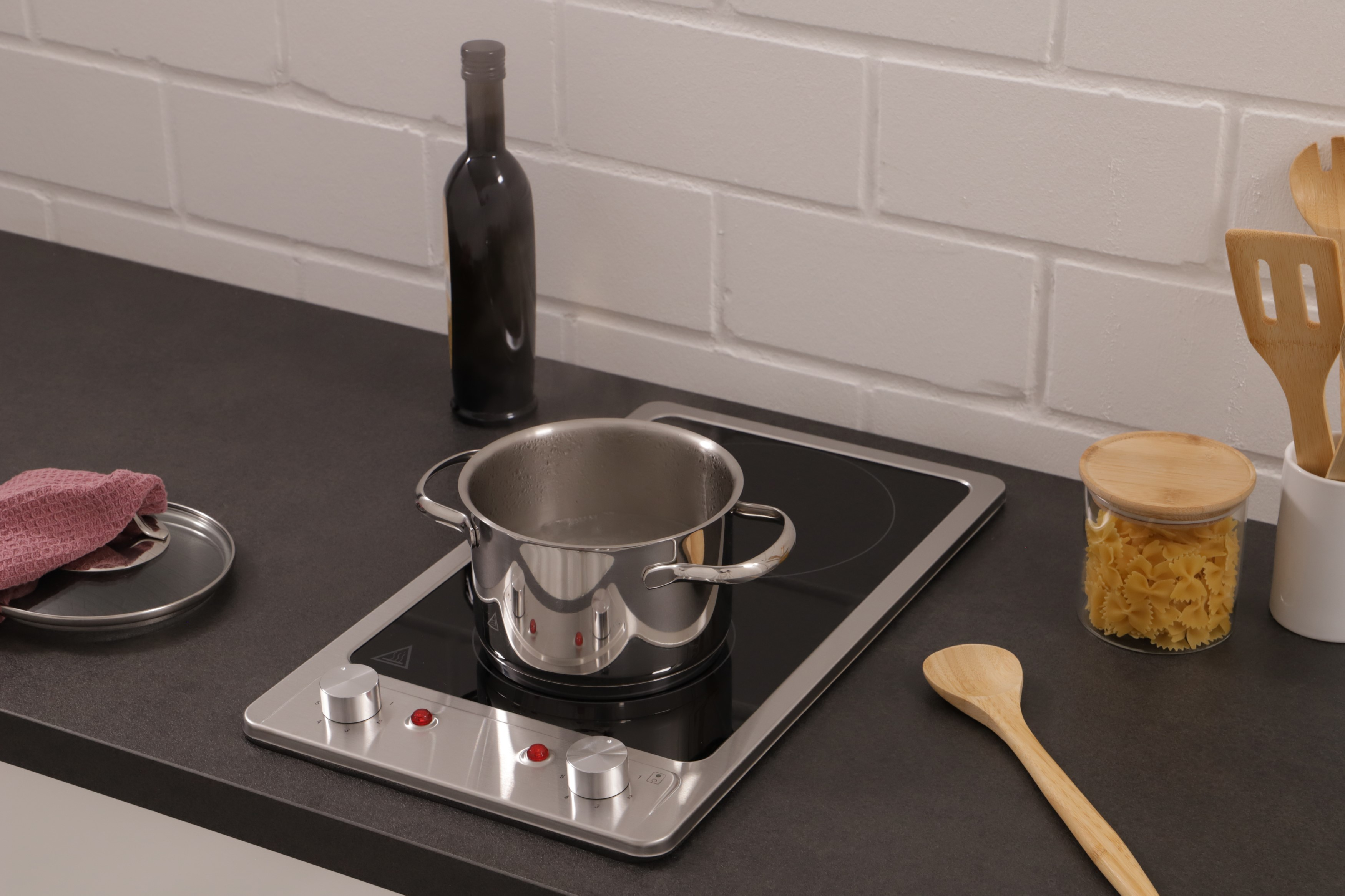 Kitchen counter with a pot on a stove, a bottle, spices, and a wooden spoon.