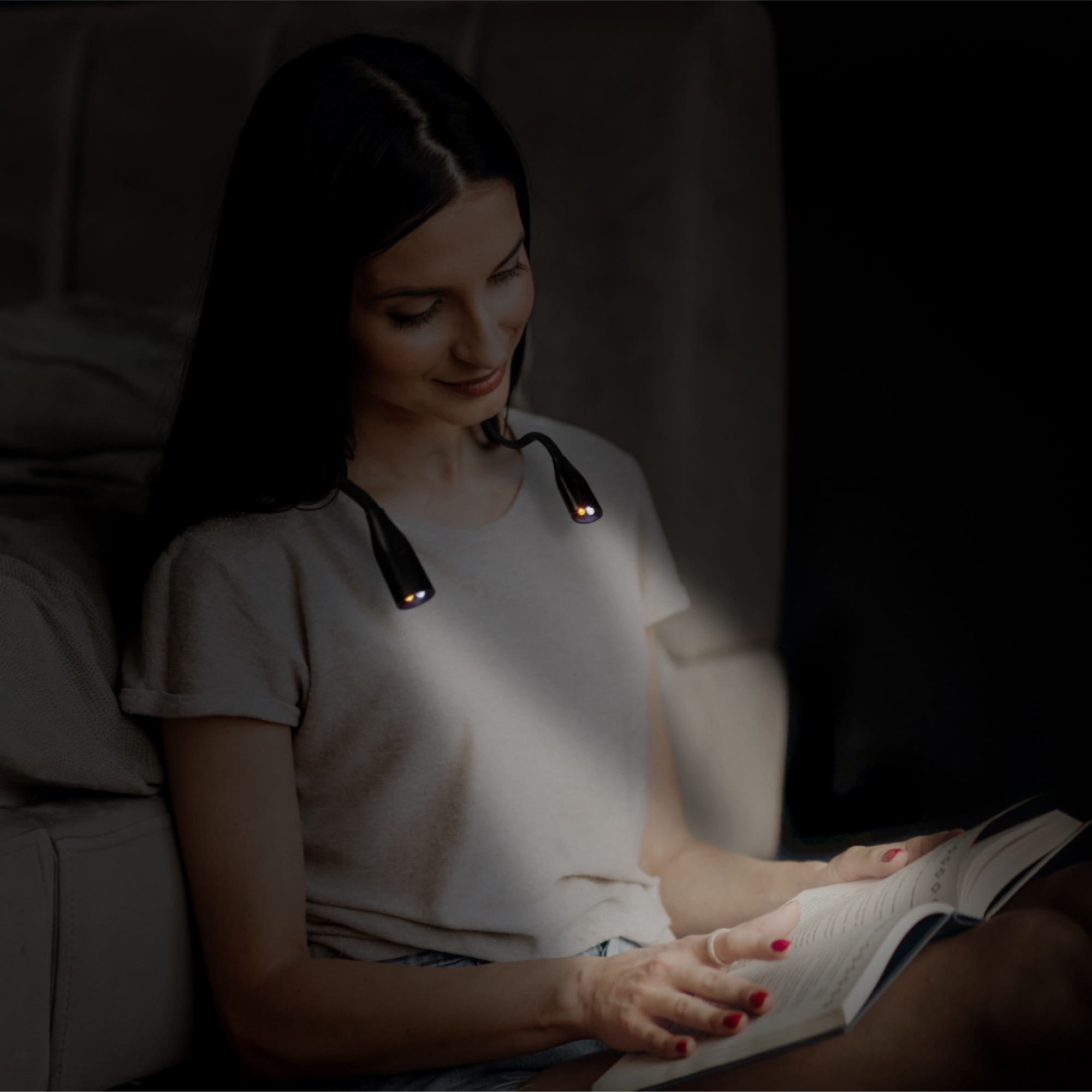 Mujer leyendo con luz de cuello, ambiente oscuro.