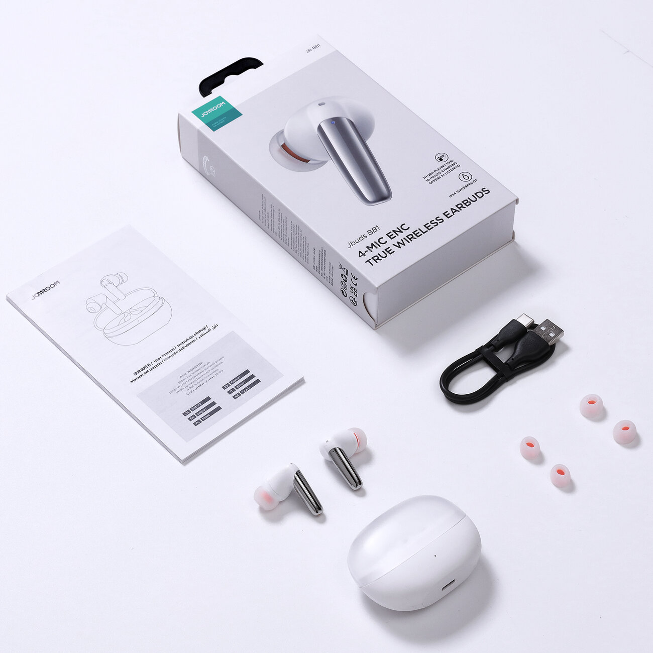 Kopfhörer-Set mit Ladecase, Ladekabel und zusätzlichen Ohrstöpseln, alles auf weißer Oberfläche.