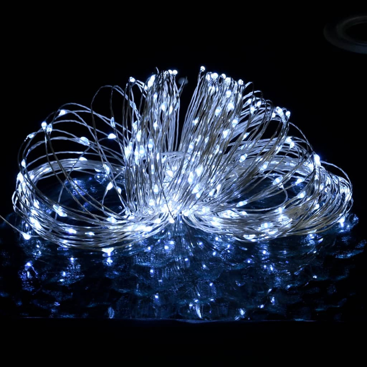 Eine Schnur aus weißen LED-Leuchten, eng gebündelt, reflektiert auf einer schwarzen Oberfläche. Die Szene ist dunkel.